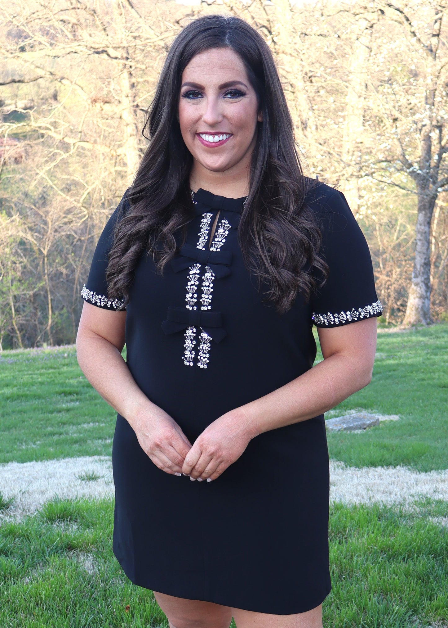 Woman wearing a black shift dress with silver embellishments outdoors.