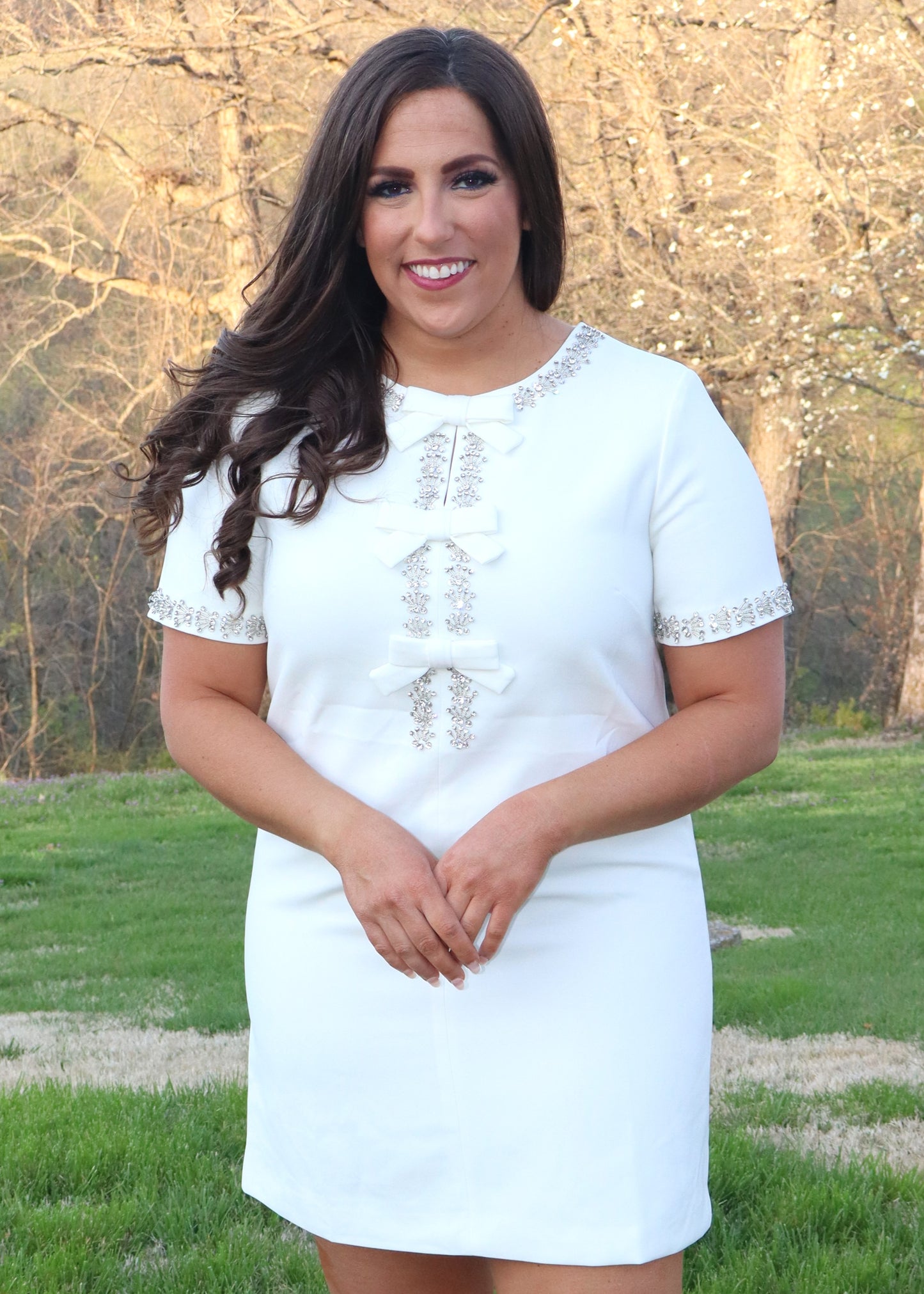Woman wearing a white shift dress with silver embellishments outdoors.