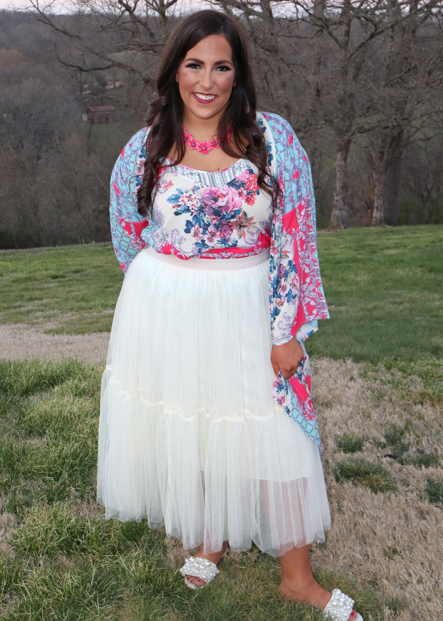 Woman wearing a matching floral top and kimono with a cream tulle skirt outdoors with trees in the background