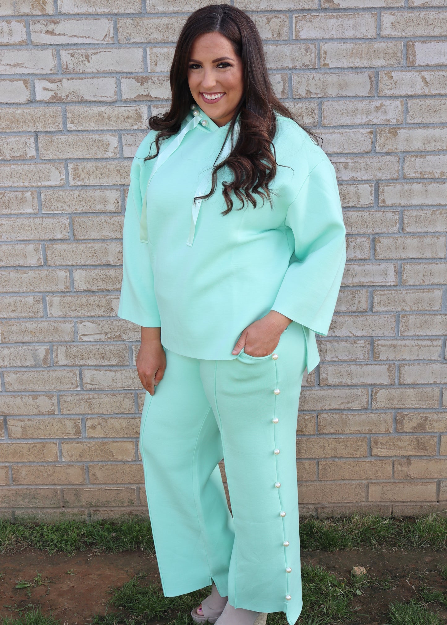 Woman wearing a mint green matching set standing next to a brick wall.