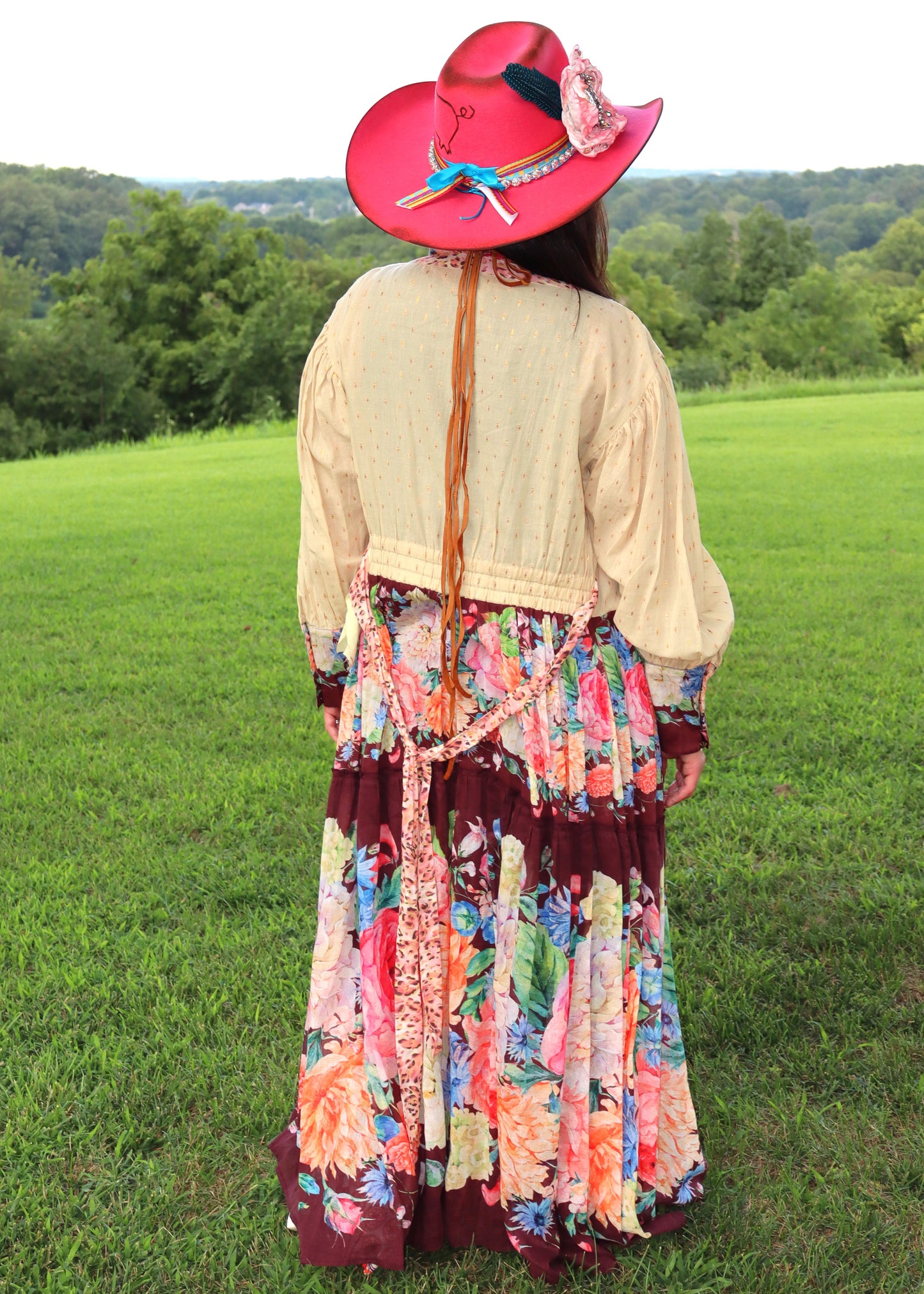 Woman in a floral dress and cowboy hat standing in a grassy field