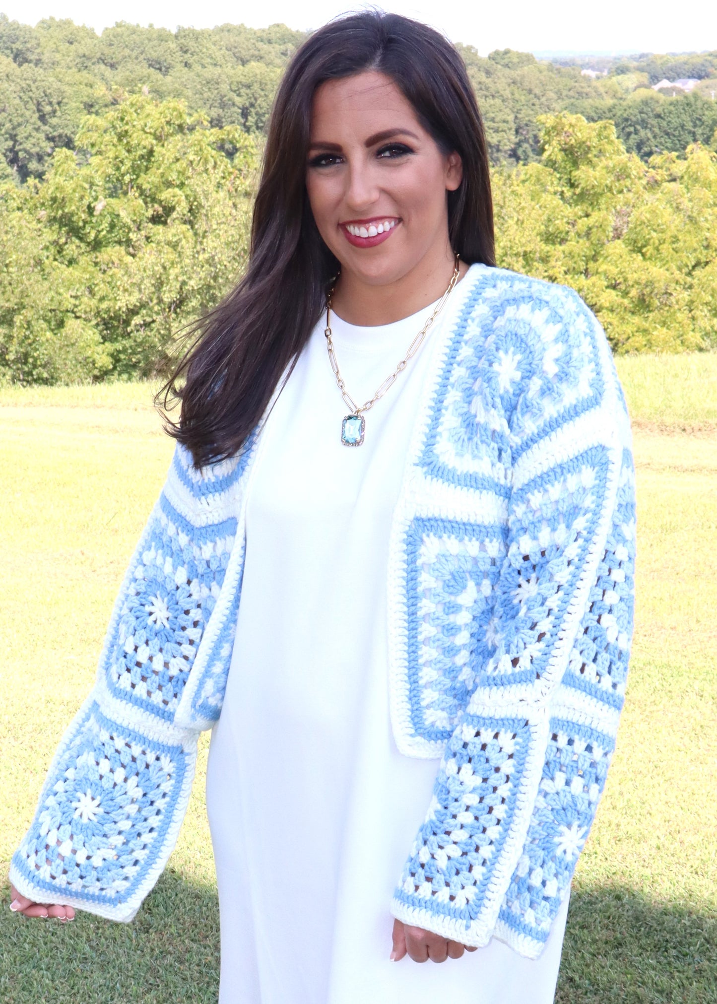 Woman wearing a blue and white crochet sweater in an outdoor setting.