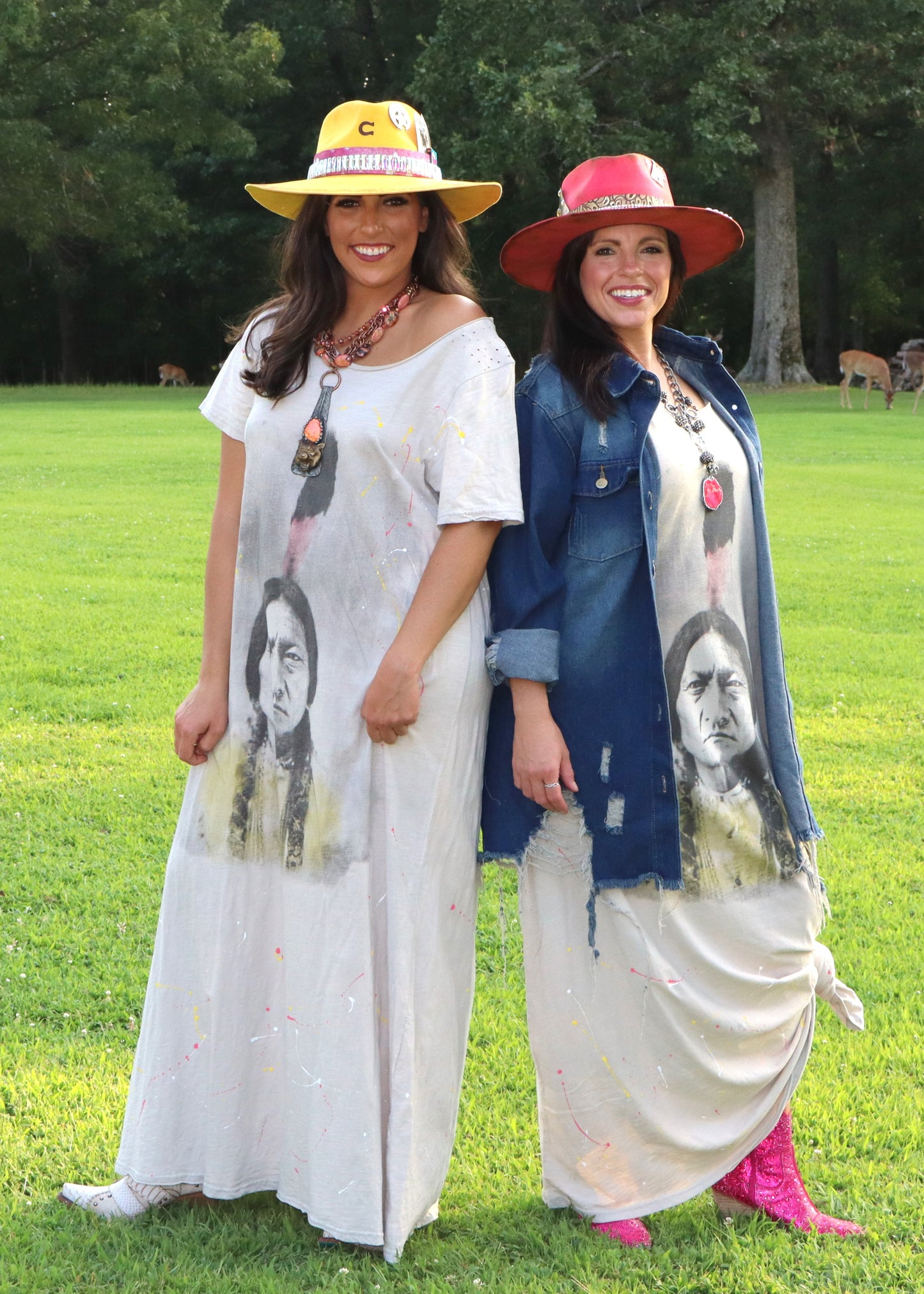 Two women wearing wide-neck dresses with an American Indian face design on a grassy field.