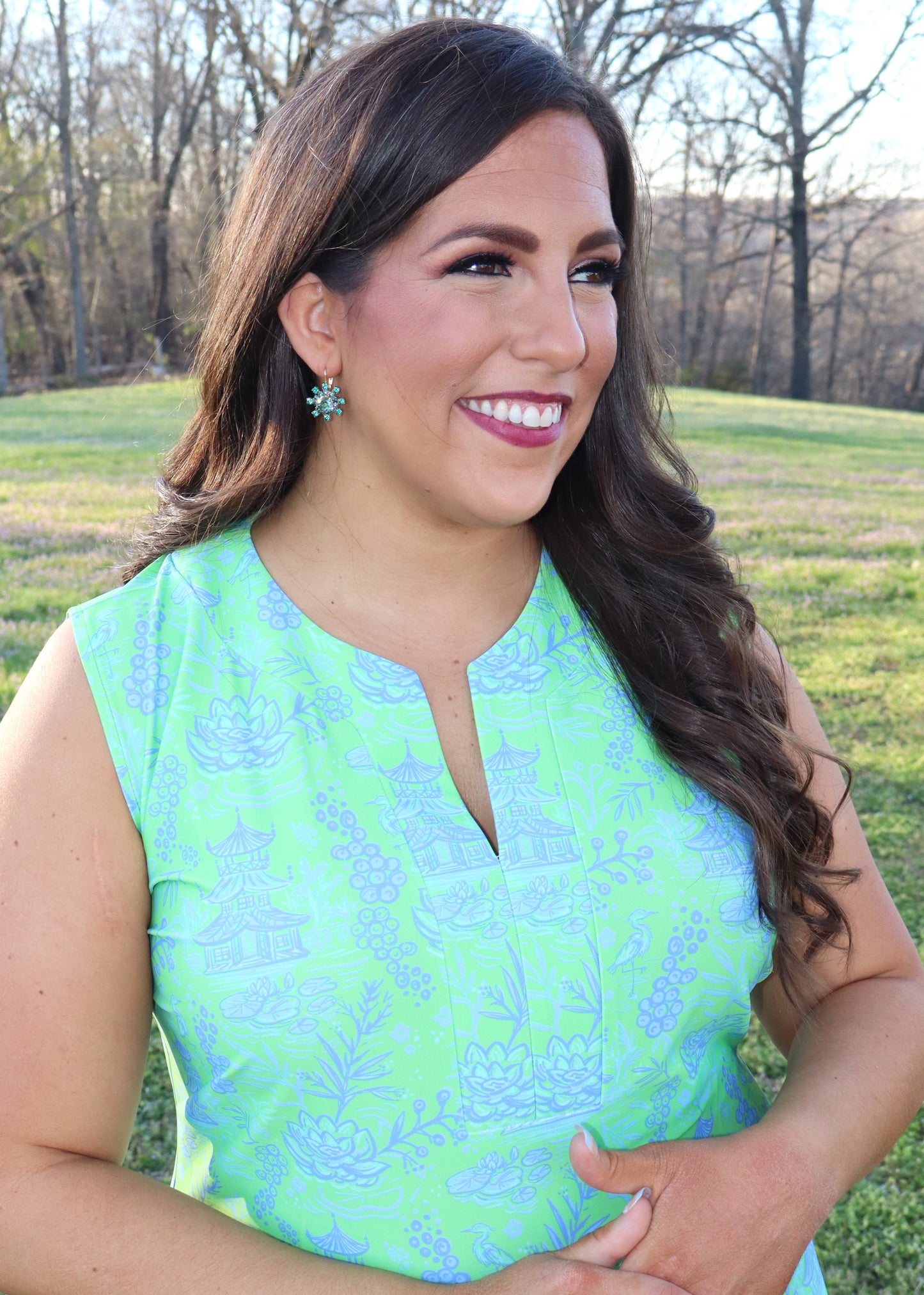 Woman wearing turquoise blue earrings and a blue and green dress standing in a grassy field.