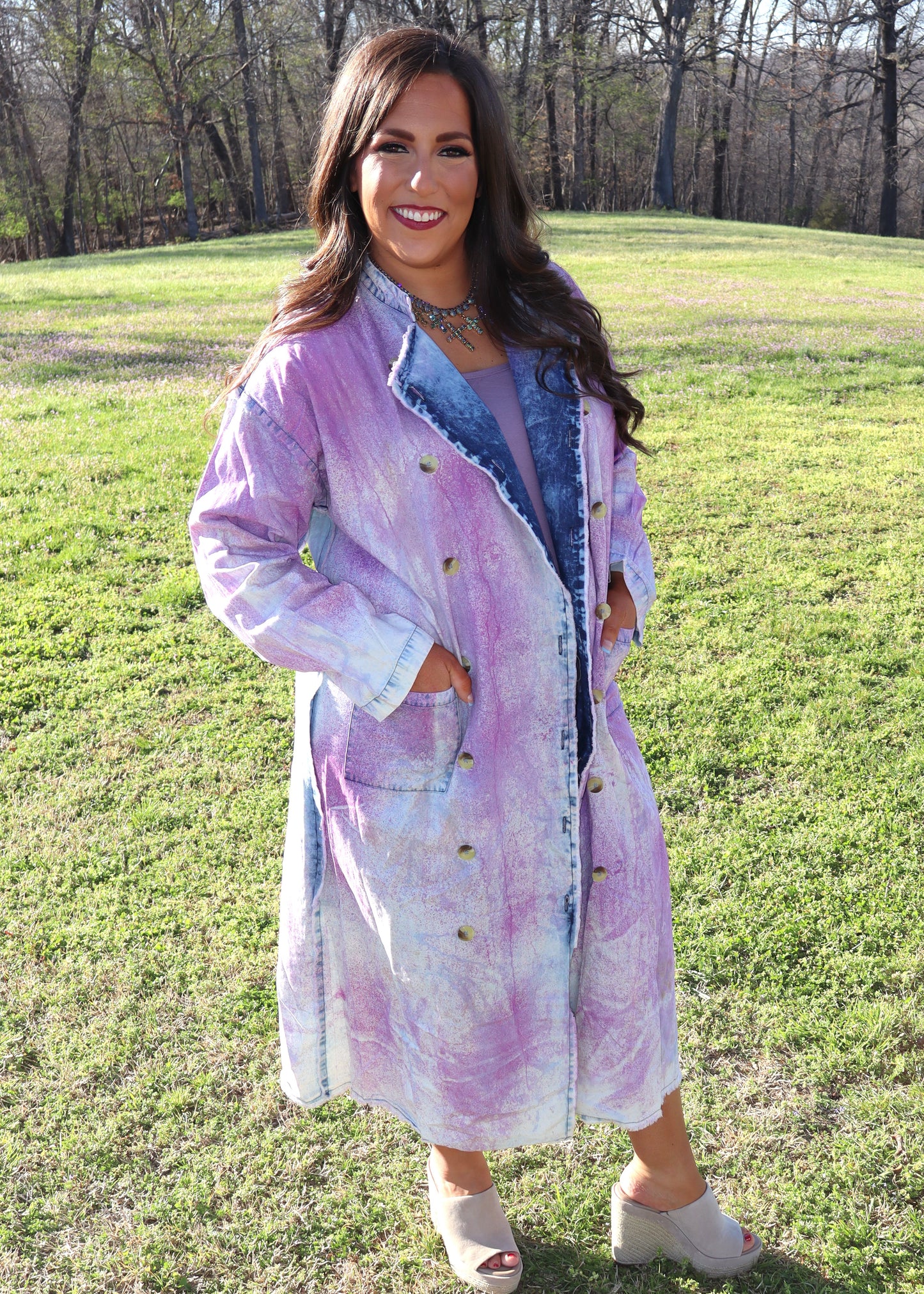 Woman wearing a purple and denim tie-dye painter's jacket outdoors on a grassy field