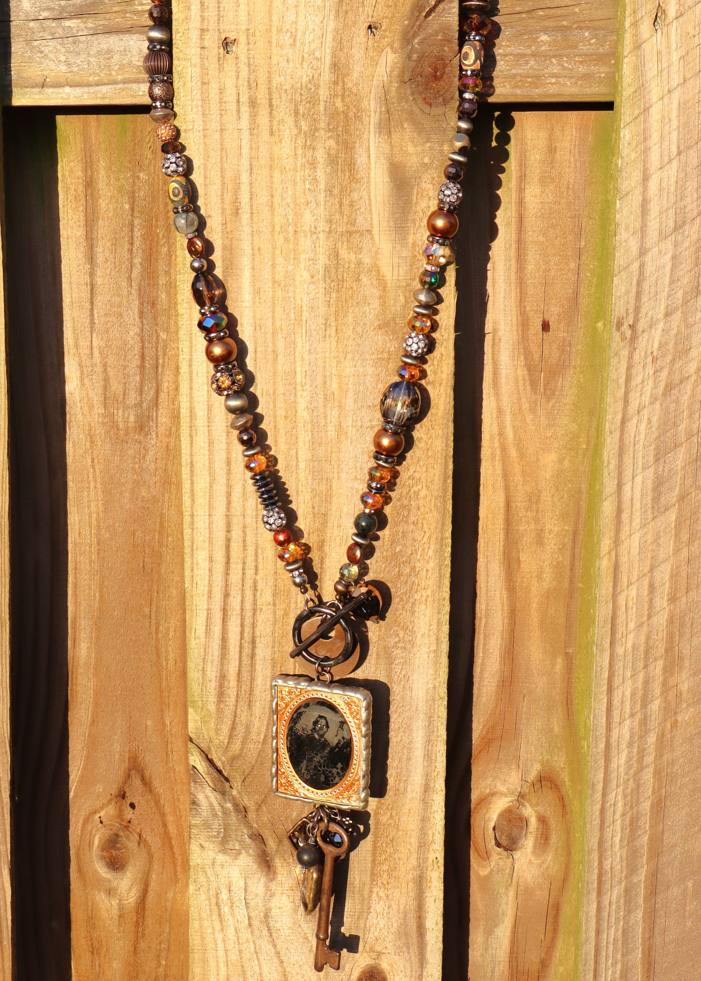 Beaded, long necklace and creepy vintage photo pendant and rustic key pendant on a wooden fence.