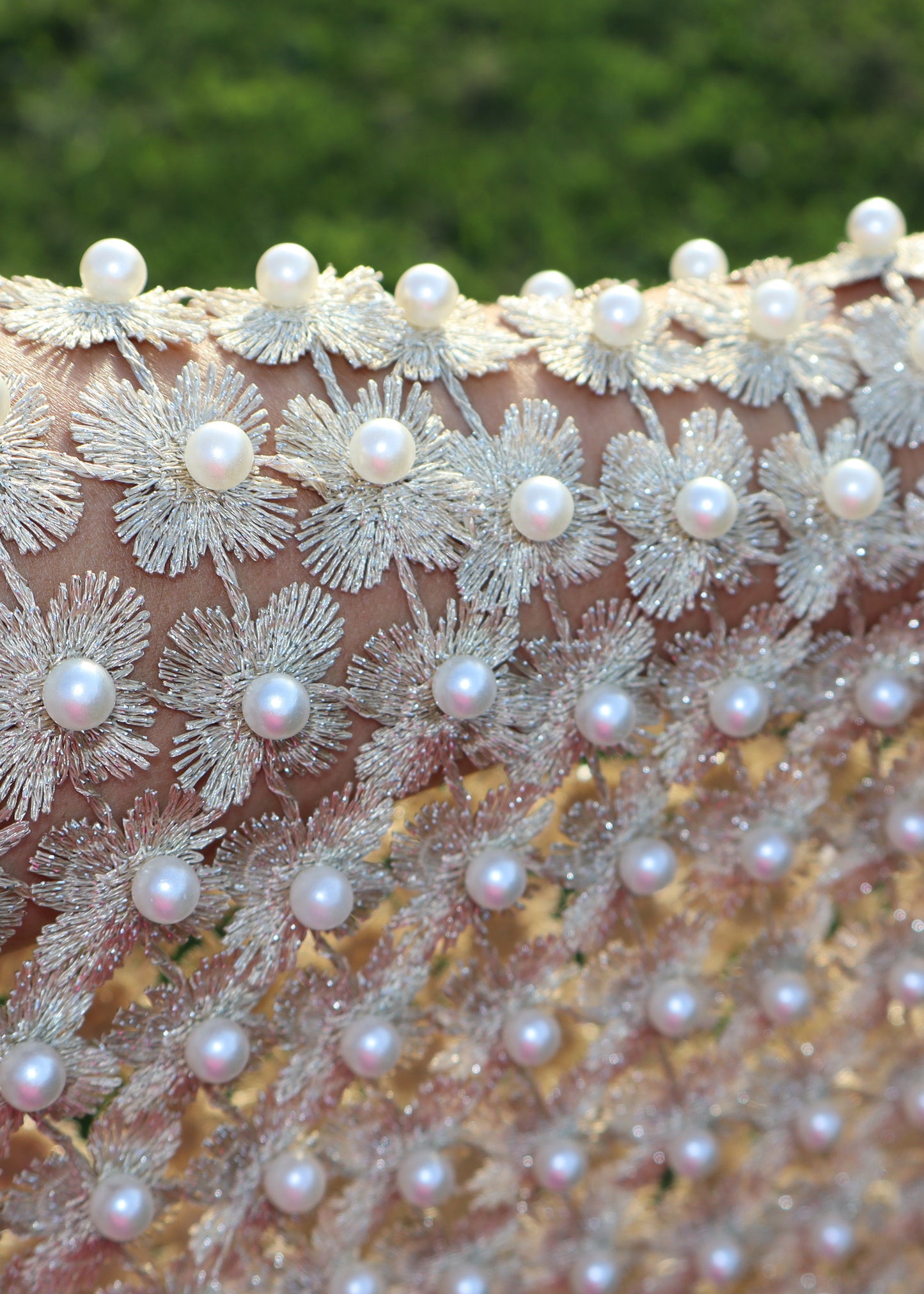 Close-up of a decorative fabric with floral patterns and pearls against a blurred green background
