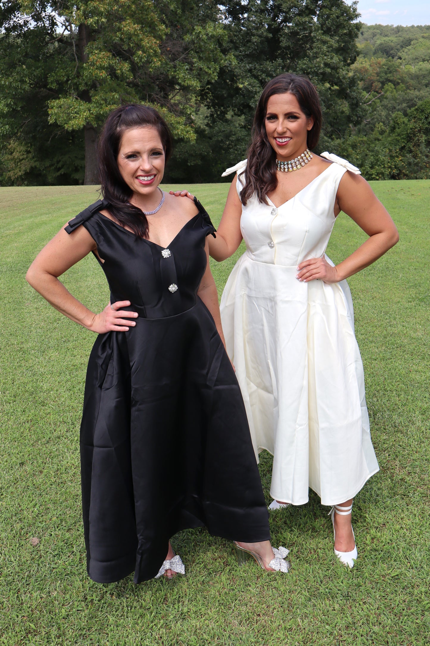 Two women wearing long dresses while standing in a field.