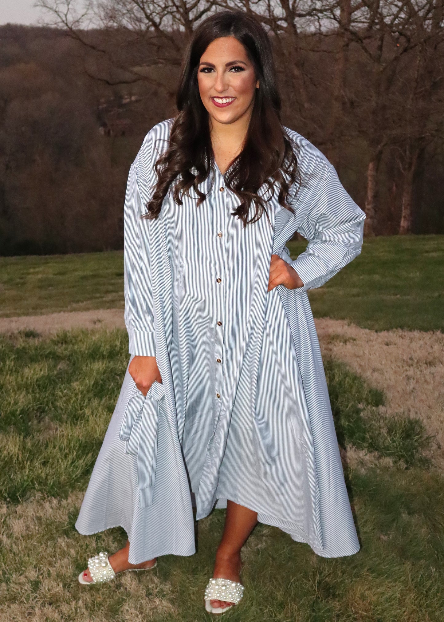 Woman wearing a black and white pin stripe dress standing outdoors with trees in the background