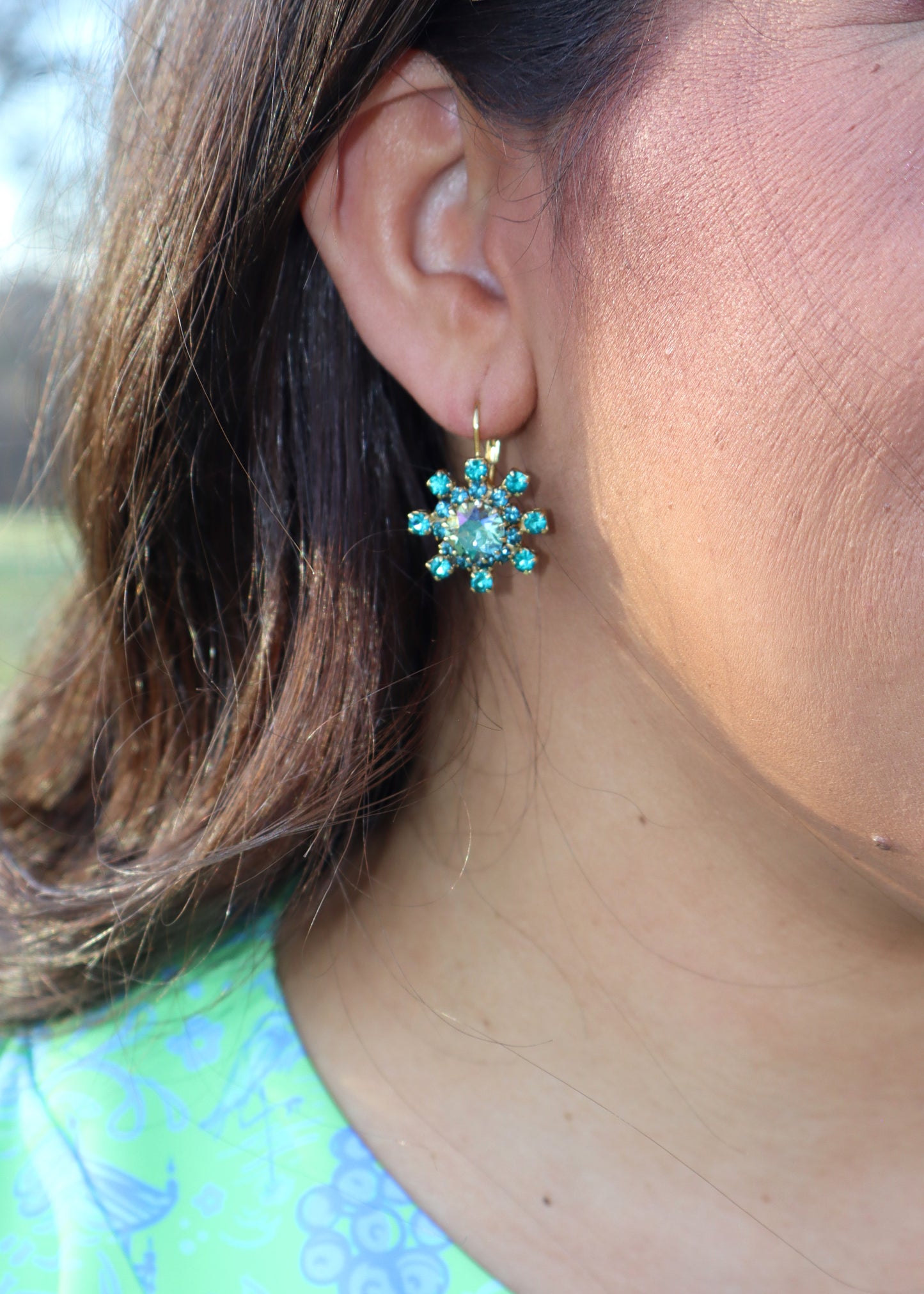 Woman wearing turquoise blue earrings and a blue and green dress standing in a grassy field.