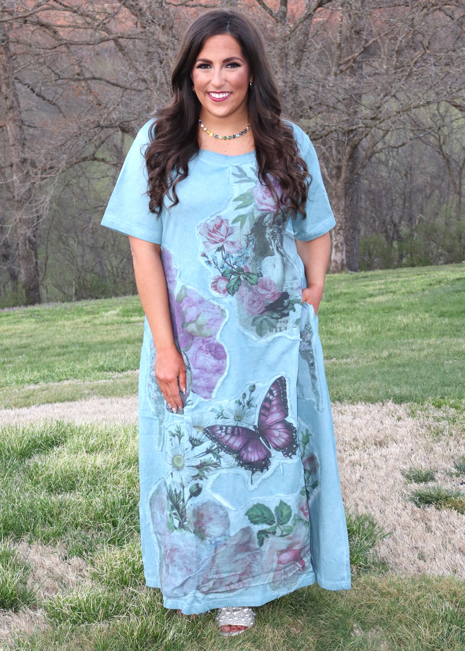 Woman wearing a light blue dress with floral, vintage lady, and butterfly patterns outdoors.