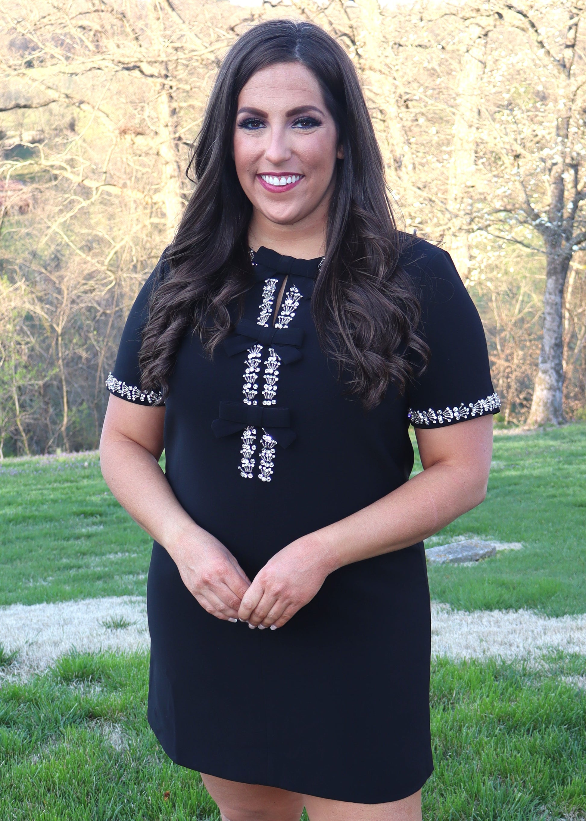 Woman wearing a black shift dress with silver embellishments outdoors.