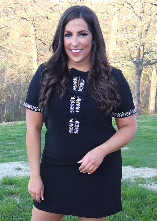 Woman wearing a black shift dress with silver embellishments outdoors.