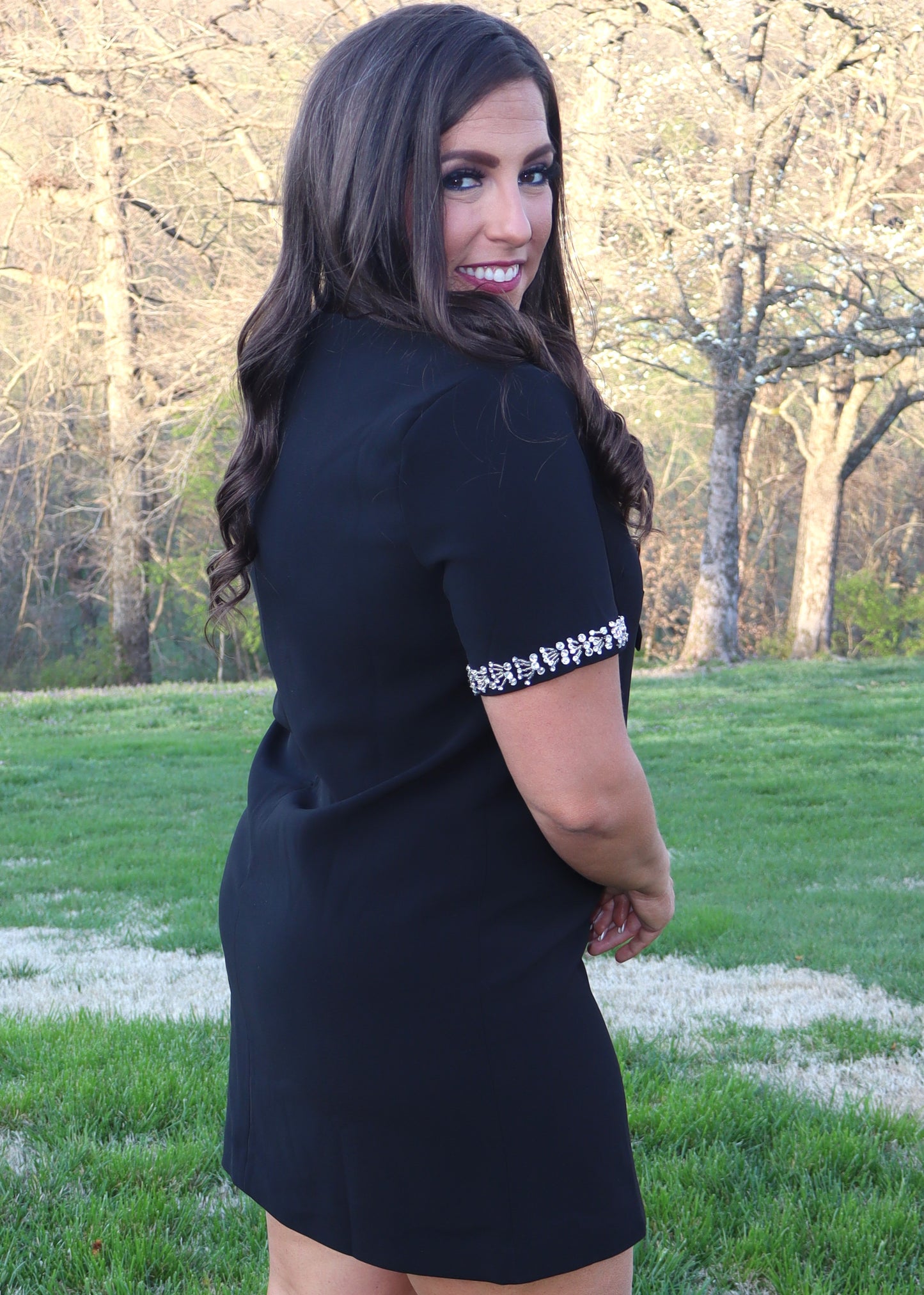 Woman wearing a black shift dress with silver embellishments outdoors.