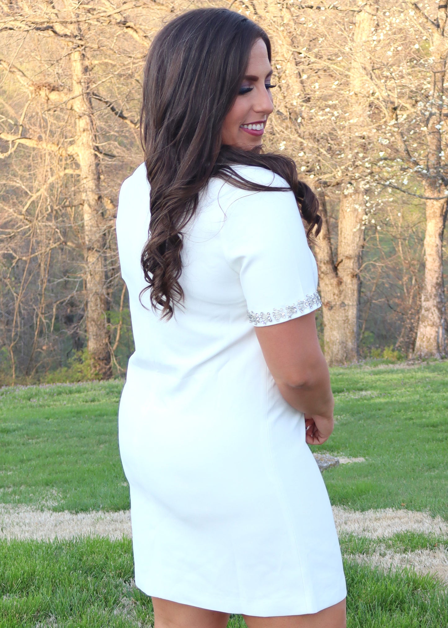 Woman wearing a white shift dress with silver embellishments outdoors.