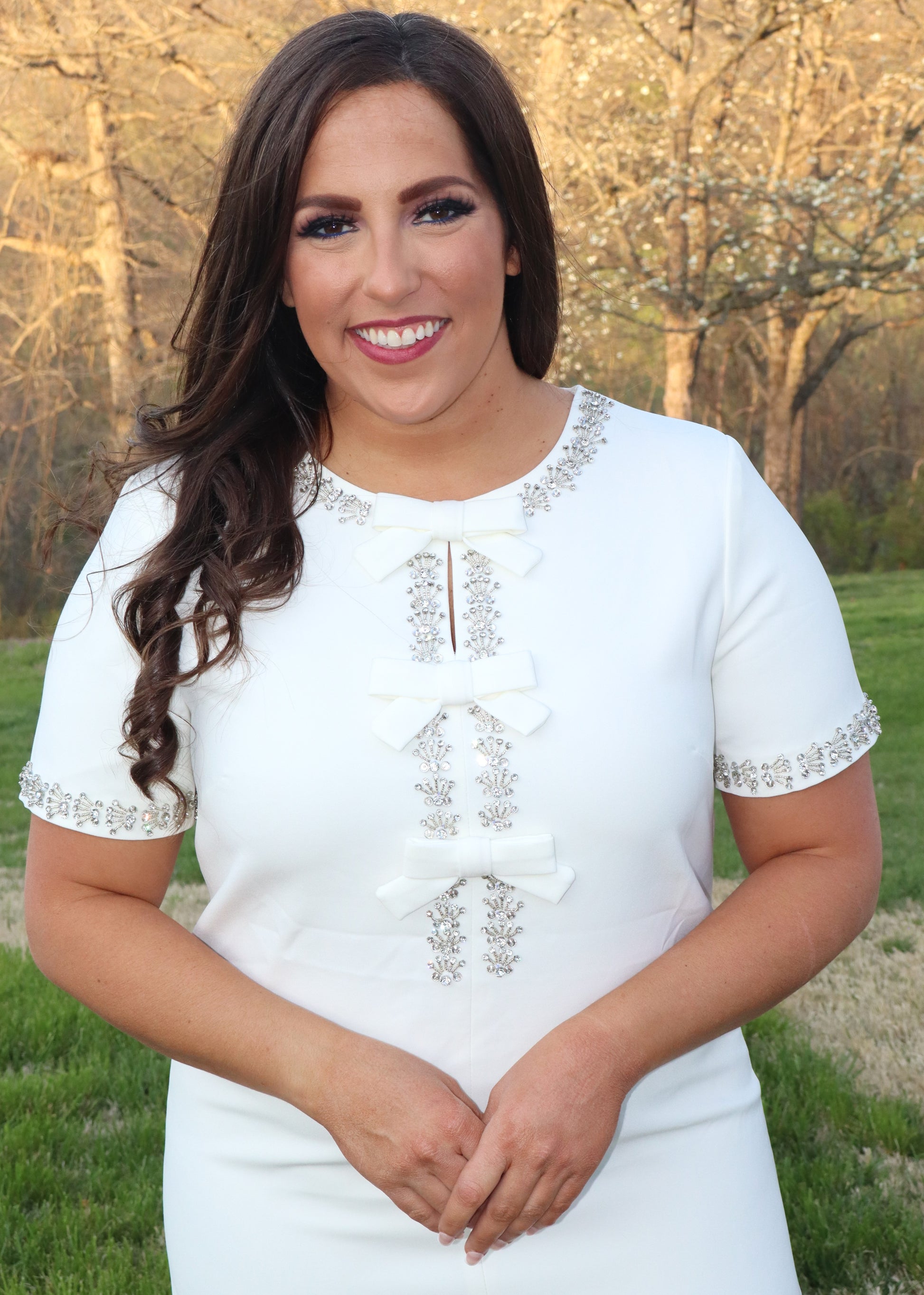 Close up of woman wearing a white shift dress with silver embellishments outdoors.