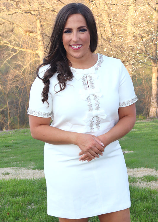 Woman wearing a white shift dress with silver embellishments outdoors.