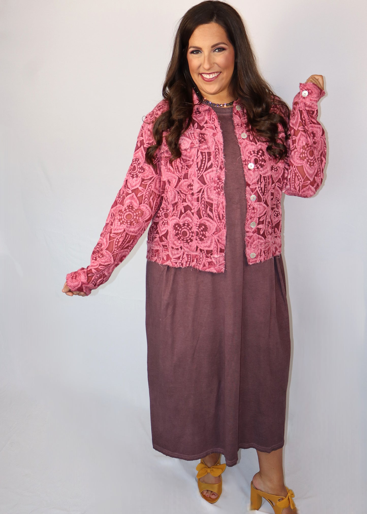 Woman wearing a pink lace cardigan over plum-colored t-shirt dress with a plain background