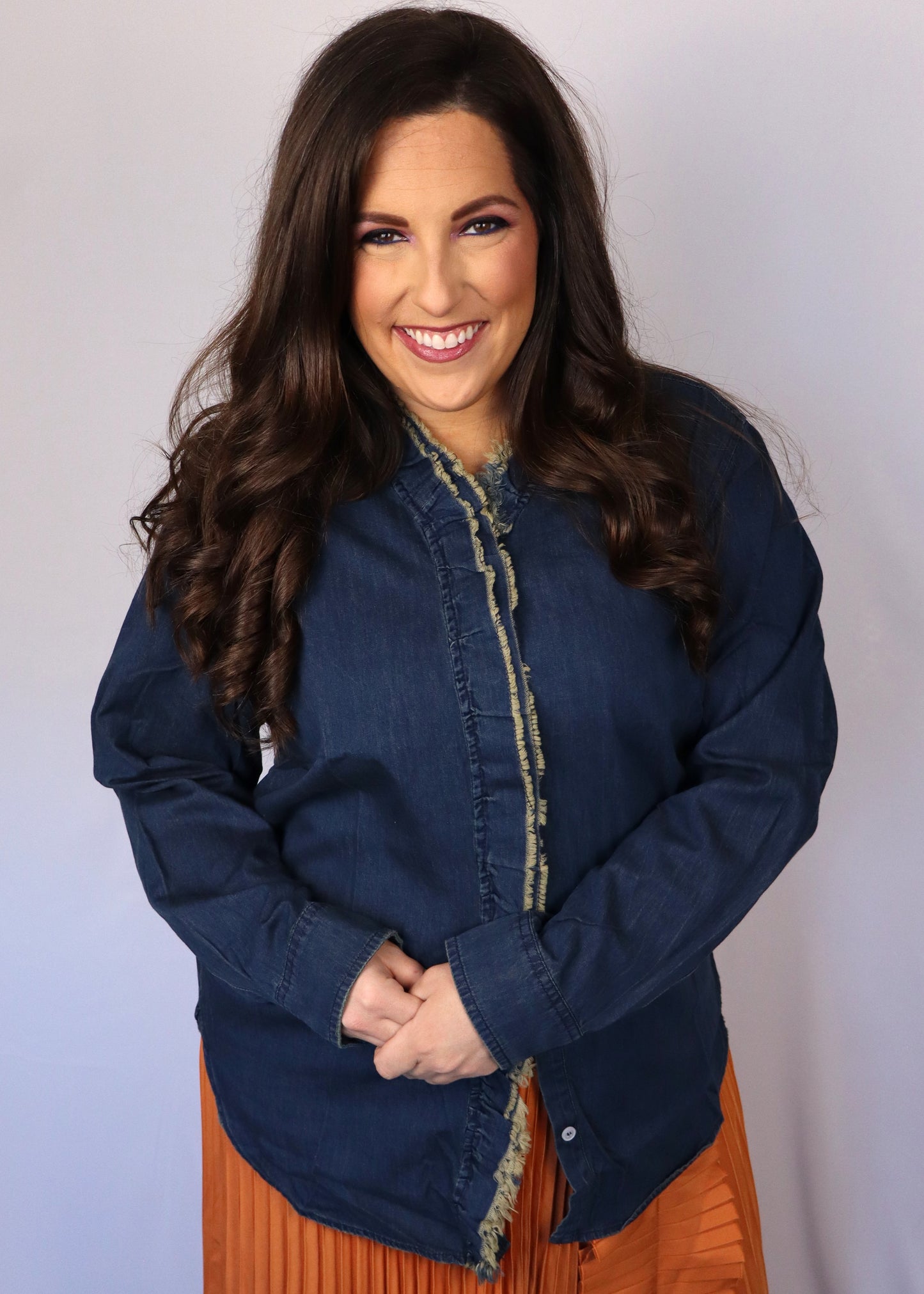 Woman wearing a dark blue denim shirt over an orange pleated skirt against a plain background
