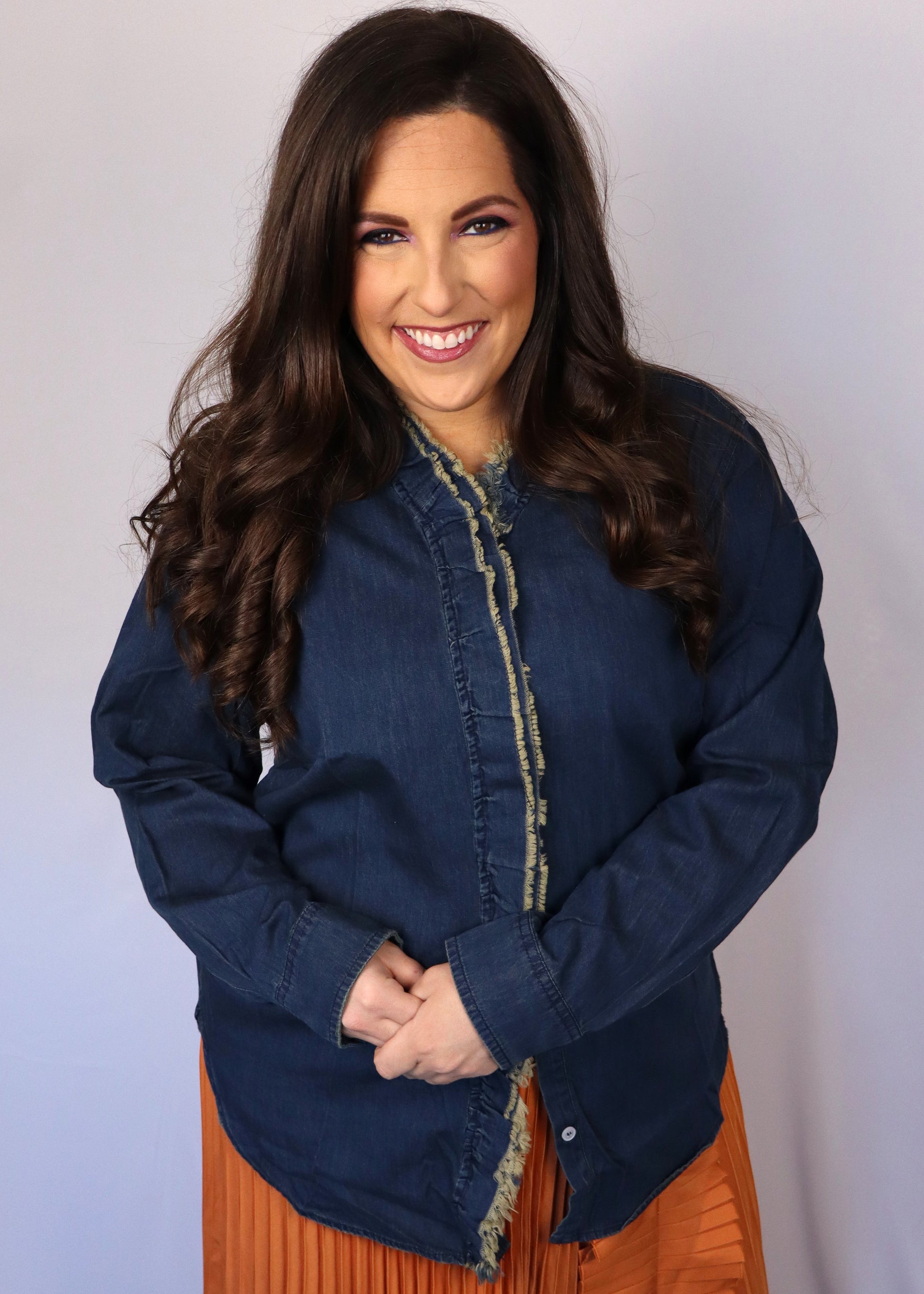 Woman wearing a dark blue denim shirt over an orange pleated skirt against a plain background