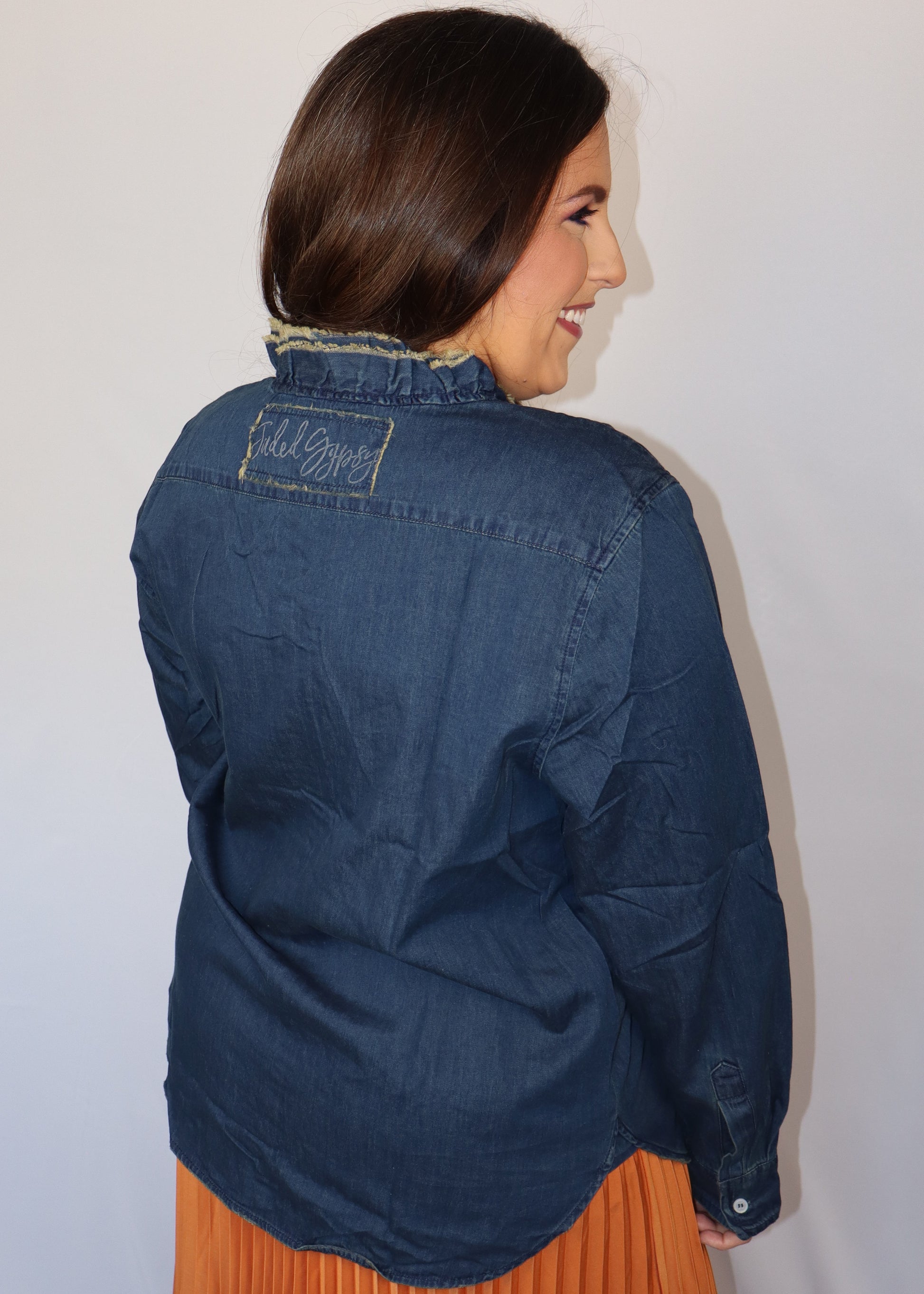 Woman wearing a dark blue denim shirt over an orange pleated skirt against a plain background