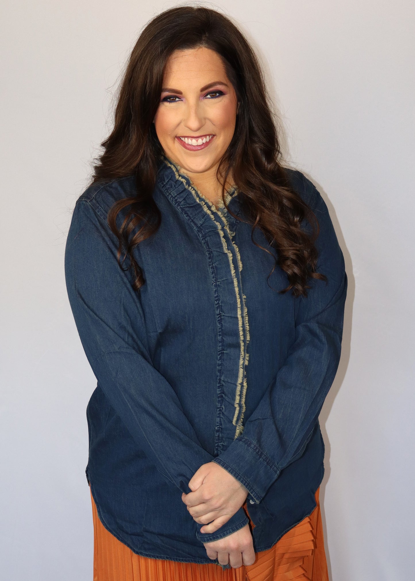 Woman wearing a dark blue denim shirt over an orange pleated skirt against a plain background