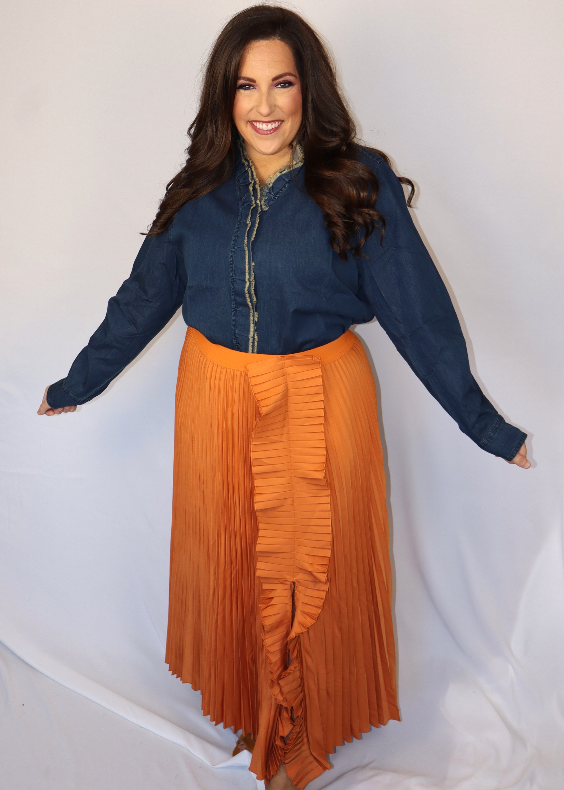 Woman wearing a denim blue top and orange pleated skirt against a white background
