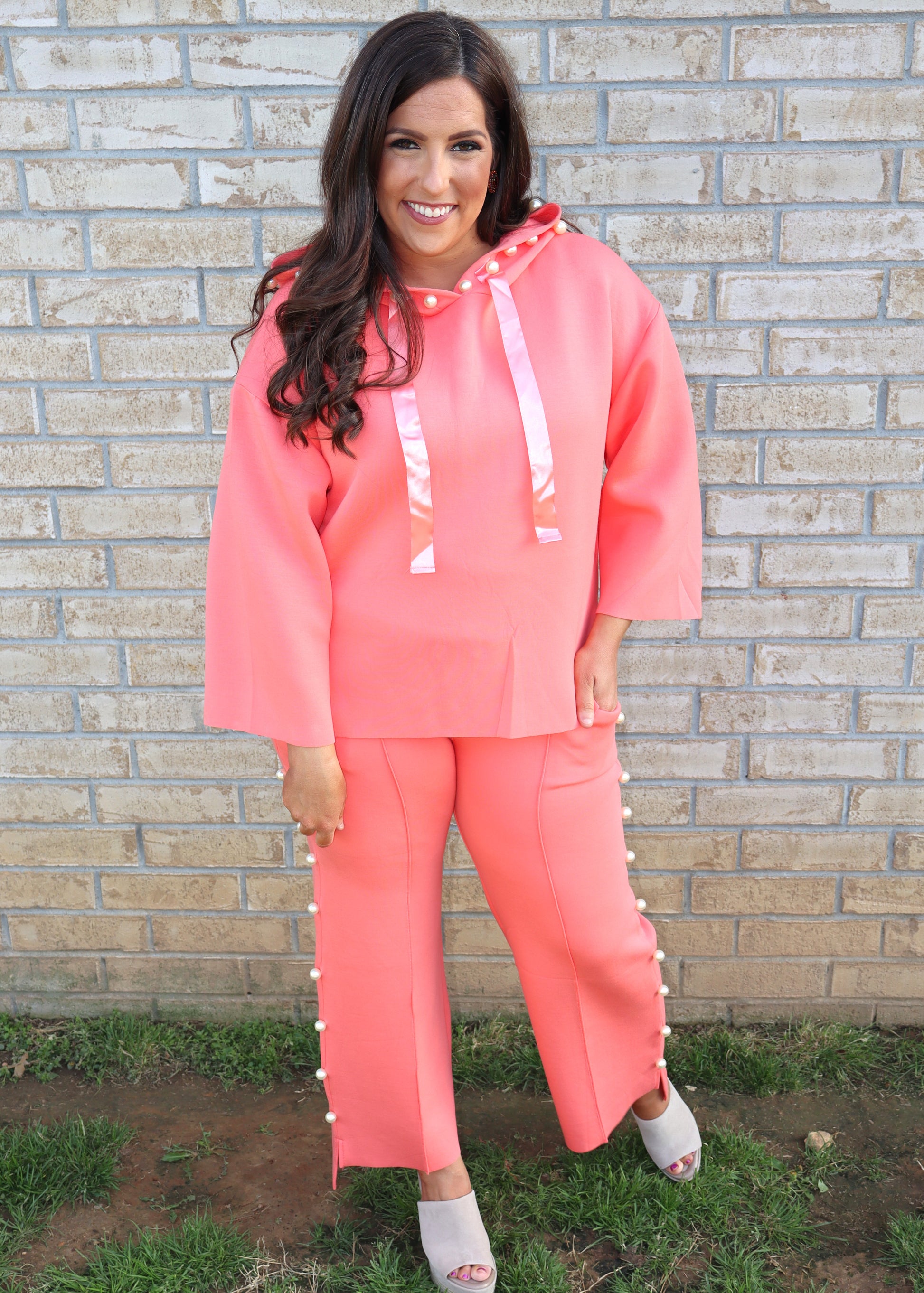 Woman wearing a coral matching set standing next to a brick wall.