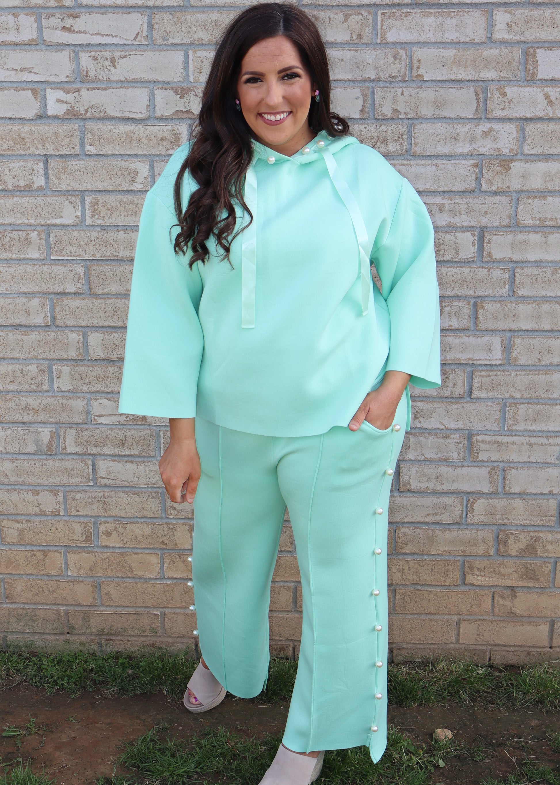 Woman wearing a mint green matching set standing next to a brick wall.