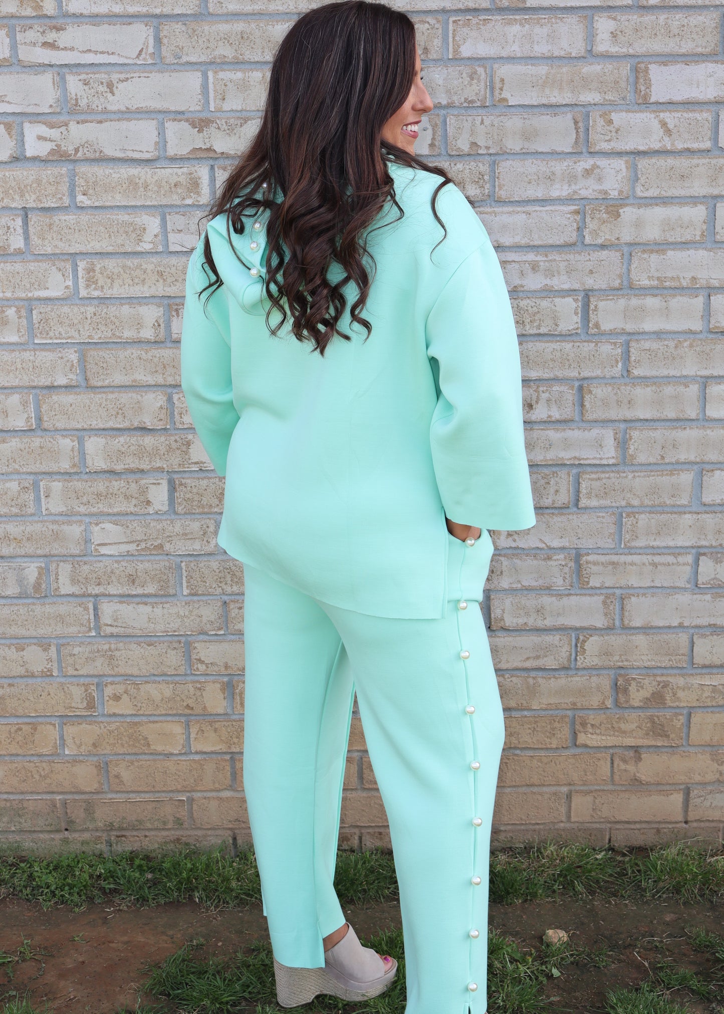 Woman wearing a mint green matching set standing next to a brick wall.