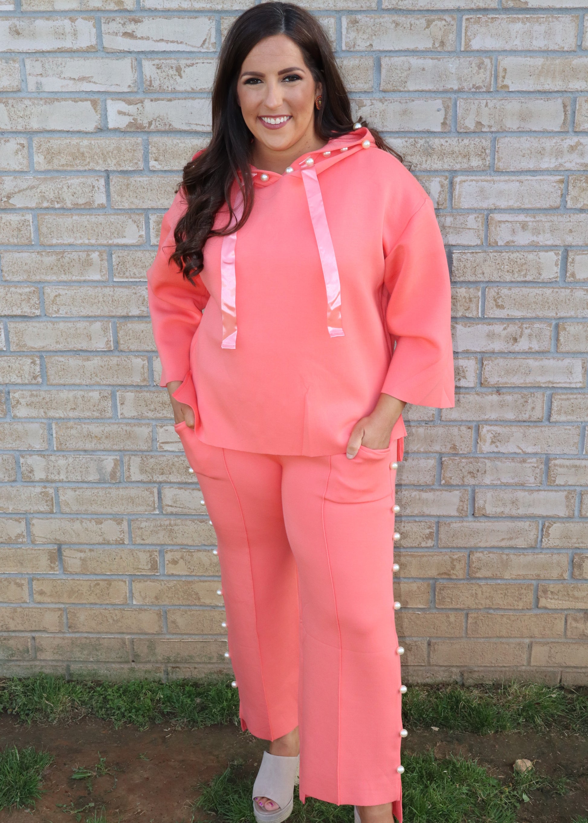 Woman wearing a coral matching set standing next to a brick wall.