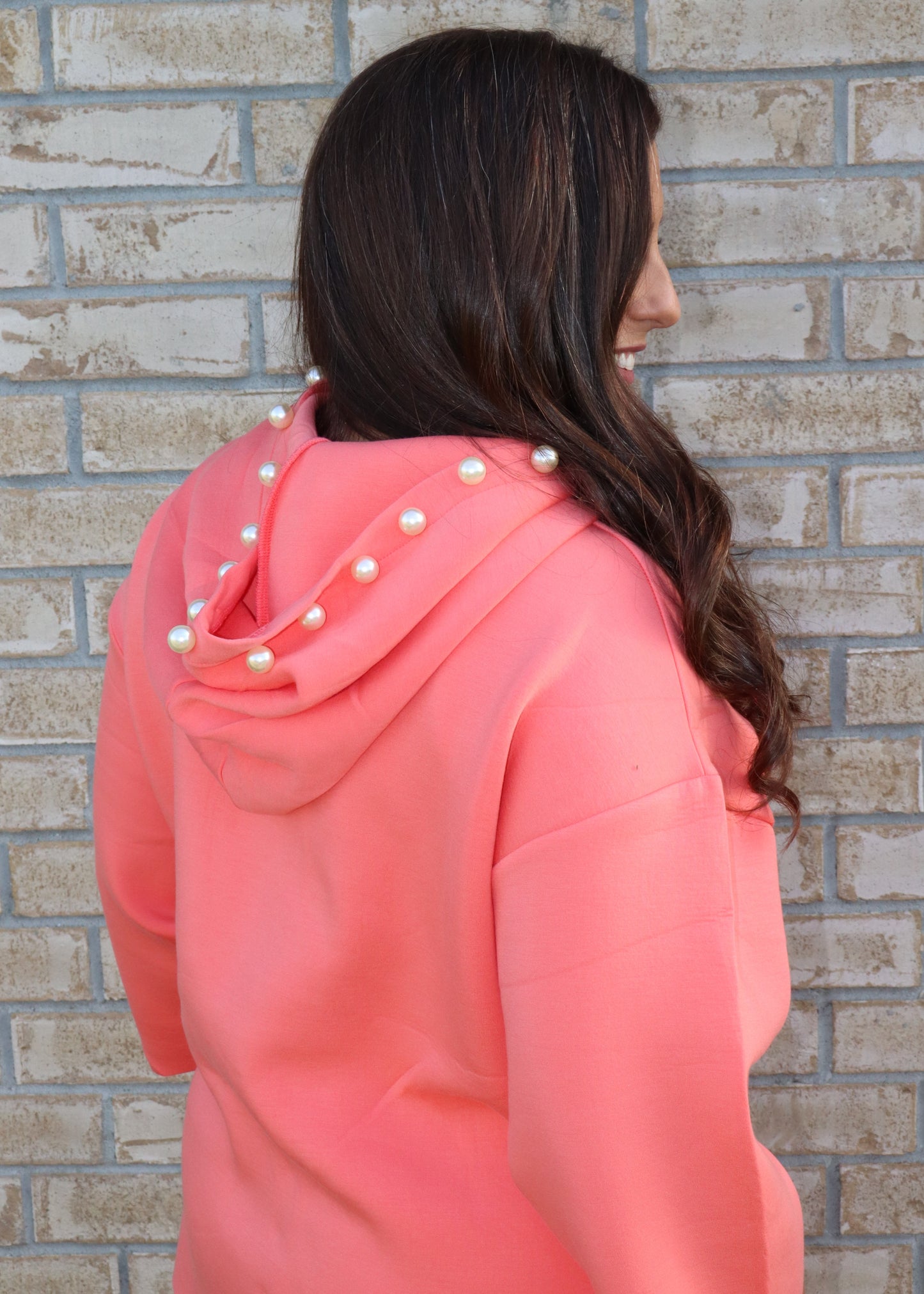 Woman wearing a coral matching set standing next to a brick wall.
