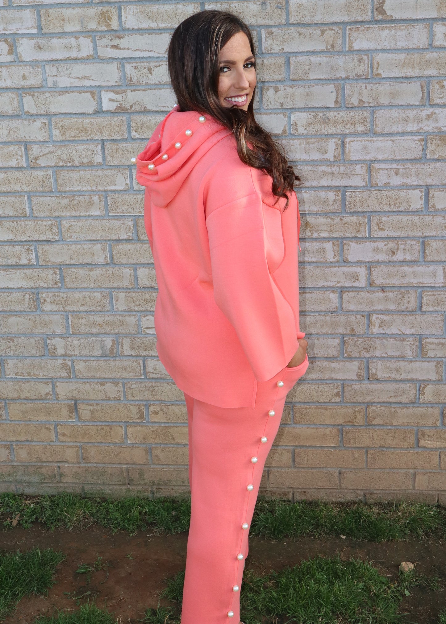 Woman wearing a coral matching set standing next to a brick wall.