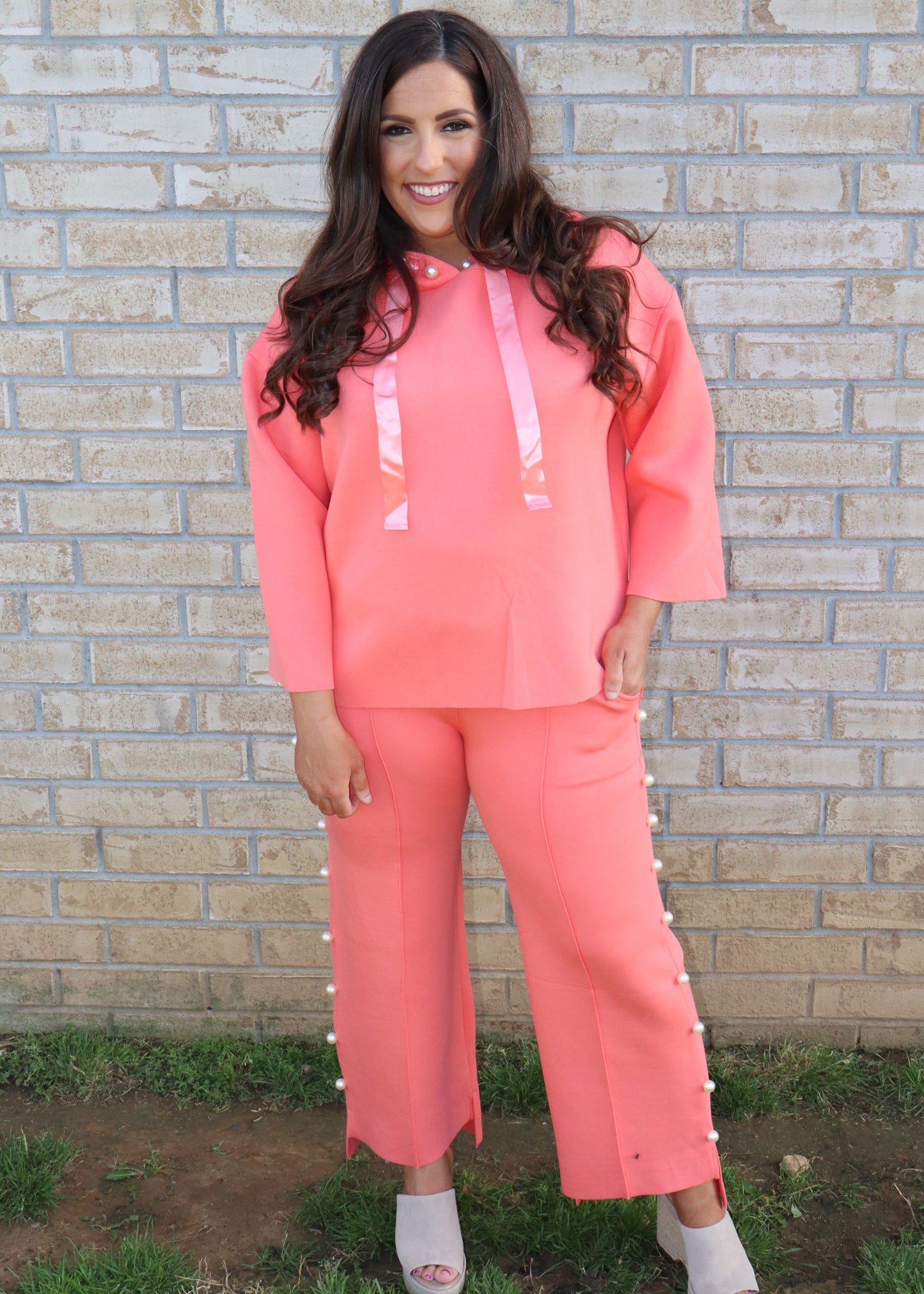 Woman wearing a coral matching set standing next to a brick wall.