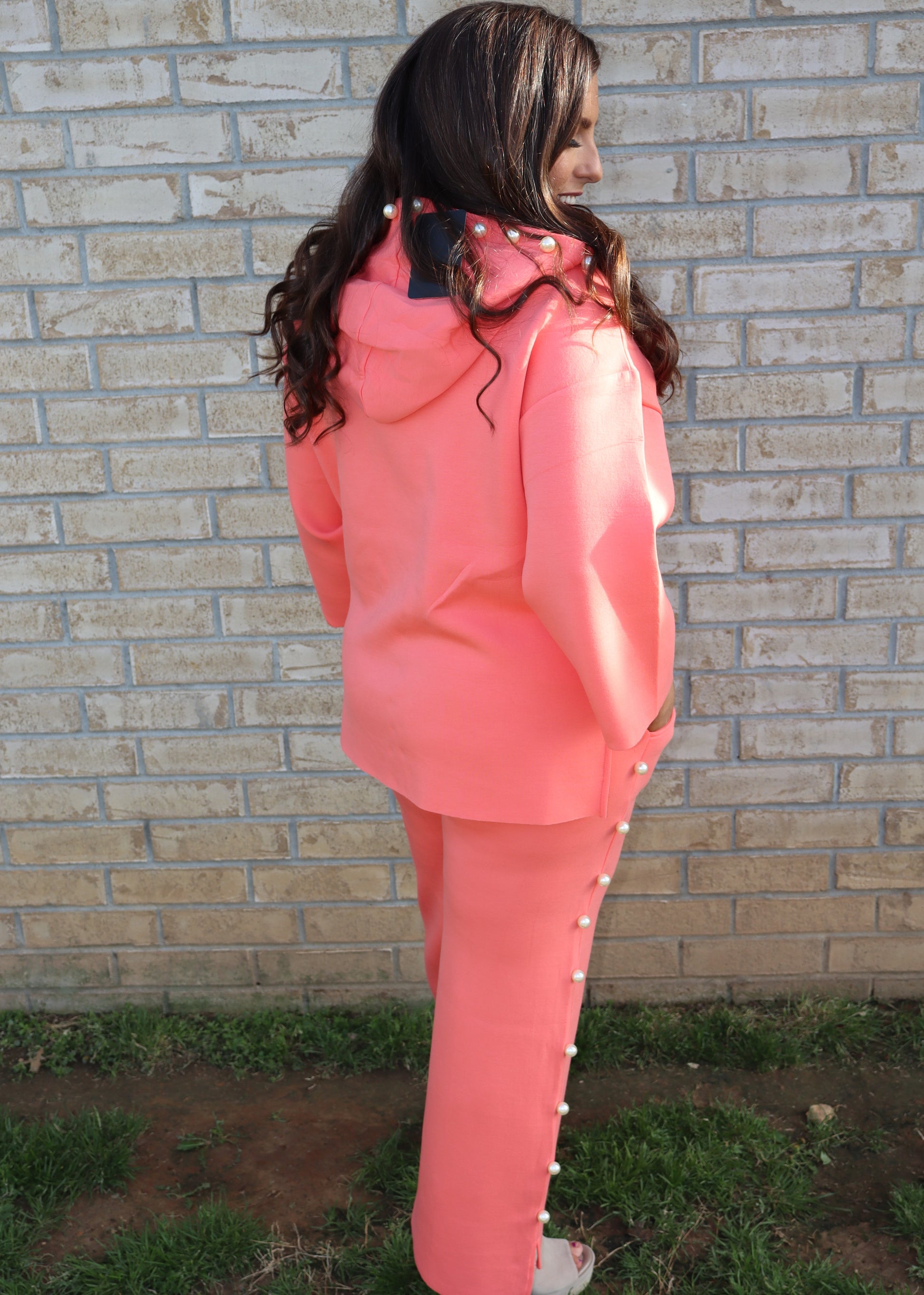 Woman wearing a coral matching set standing next to a brick wall.