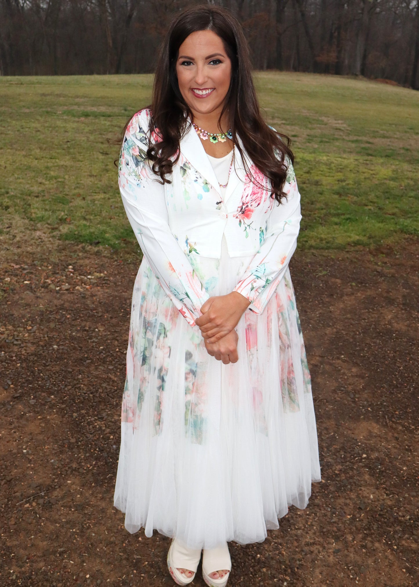 Woman wearing a white floral duster standing in a natural setting with grass and dirt.