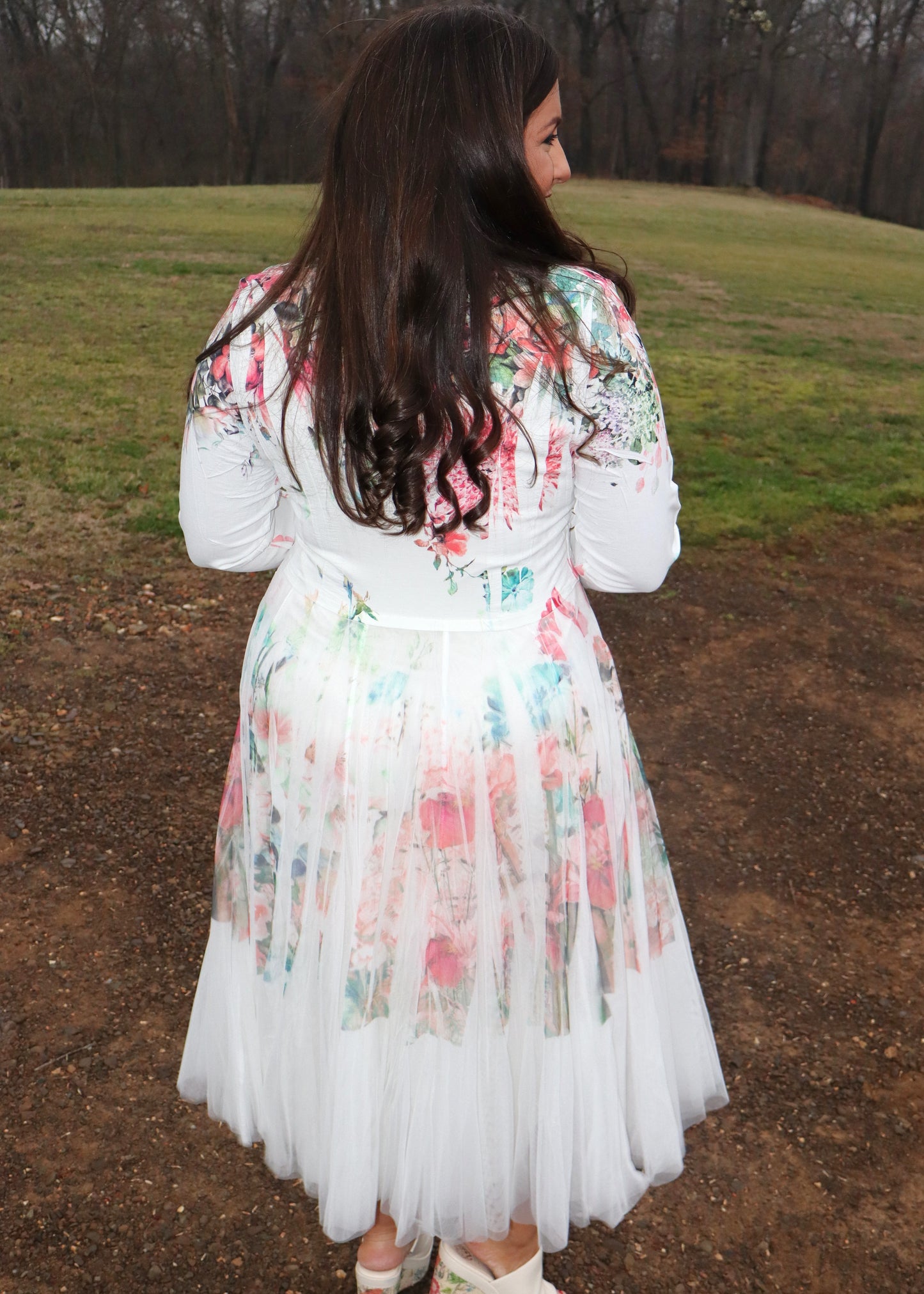 Woman wearing a white floral duster standing in a natural setting with grass and dirt.