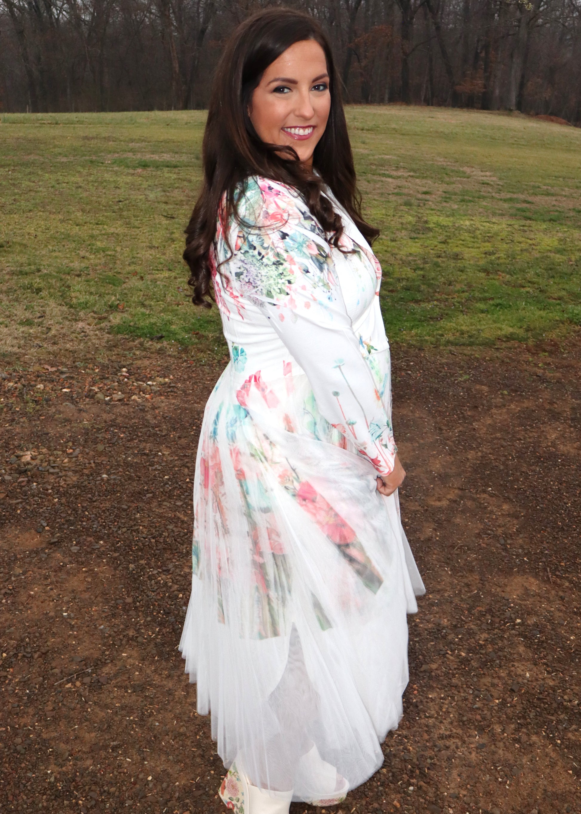 Woman wearing a white floral duster standing in a natural setting with grass and dirt.