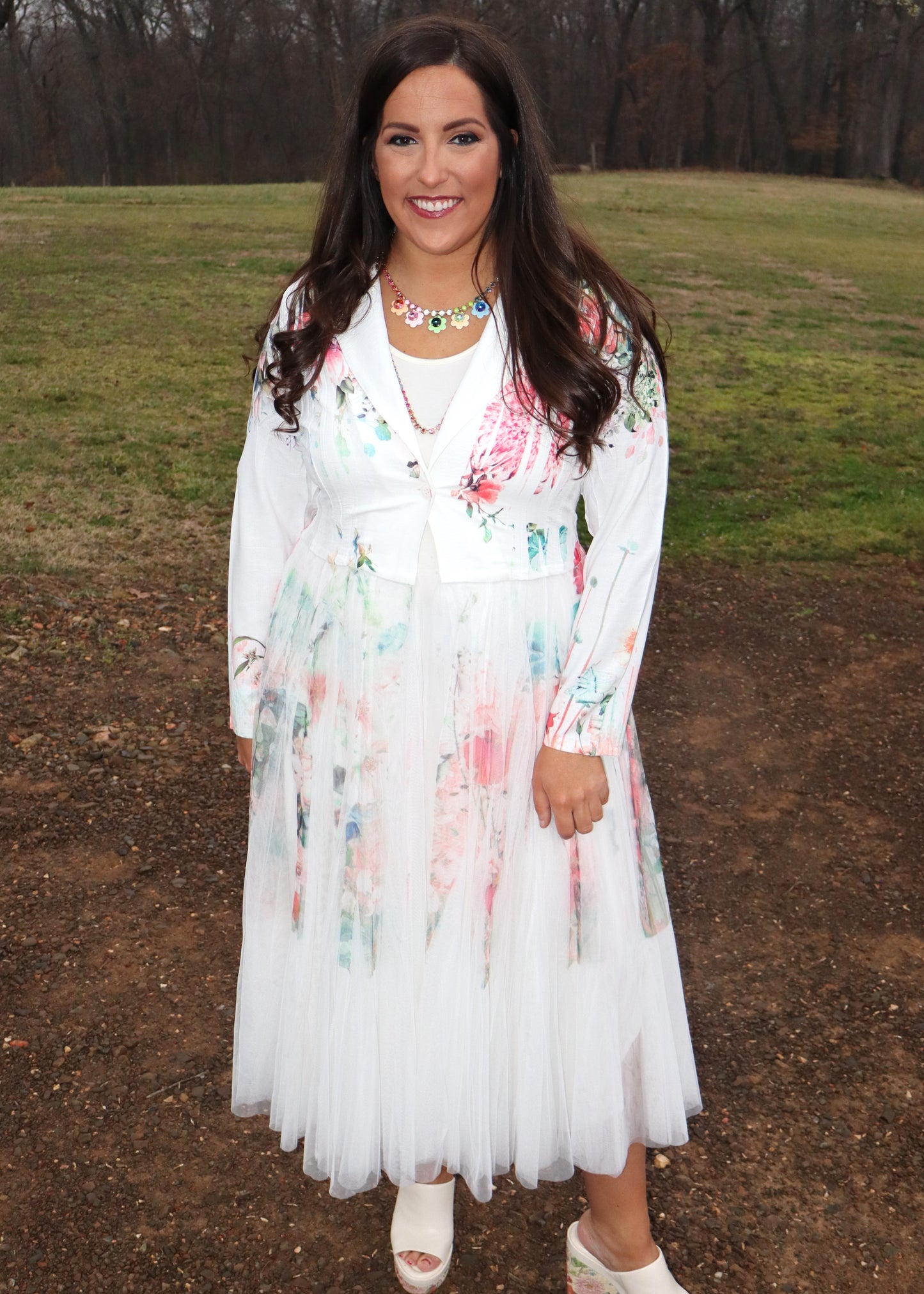 Woman wearing a white floral duster standing in a natural setting with grass and dirt.
