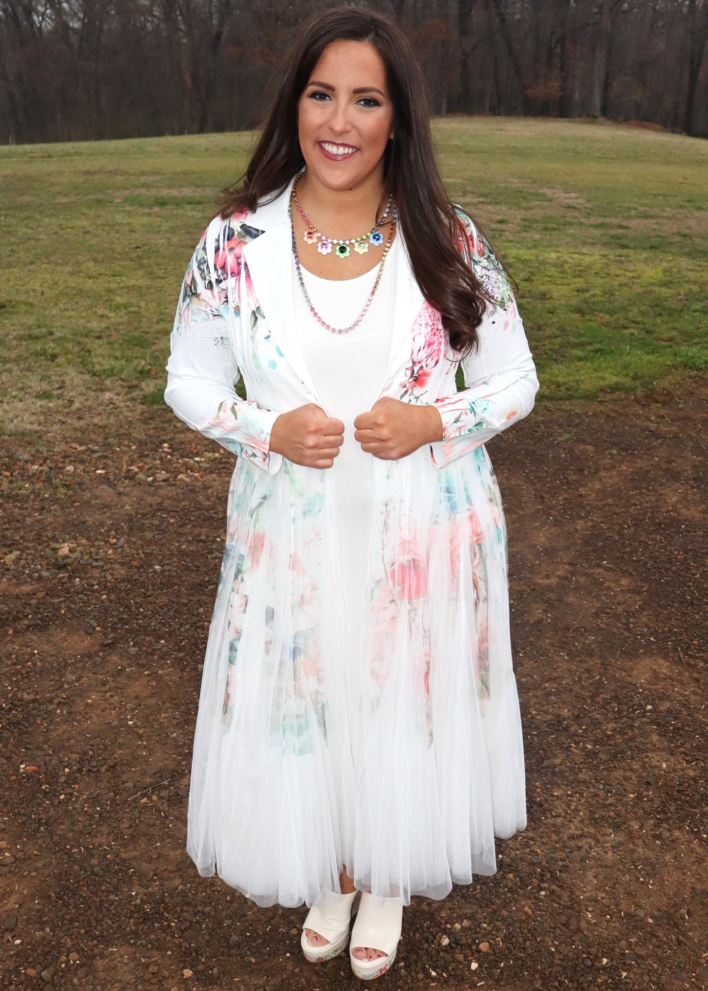 Woman wearing a white floral duster standing in a natural setting with grass and dirt.