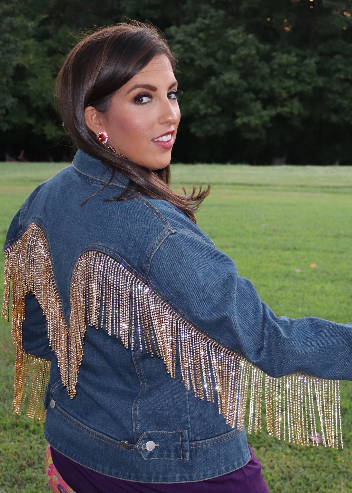 Woman wearing a blue denim jacket with gold rhinestone fringe in an outdoor setting