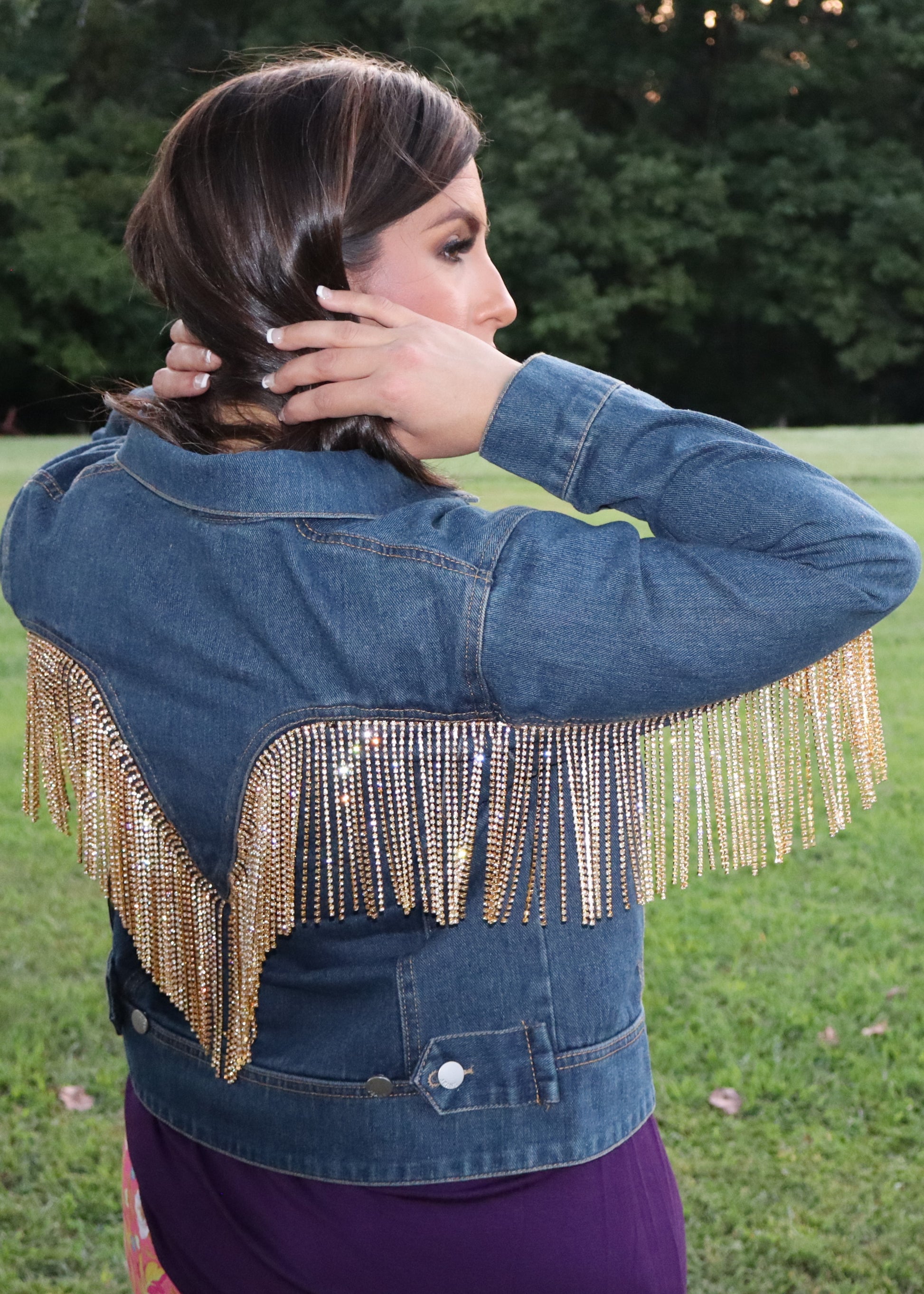 Woman wearing a blue denim jacket with gold rhinestone fringe in an outdoor setting