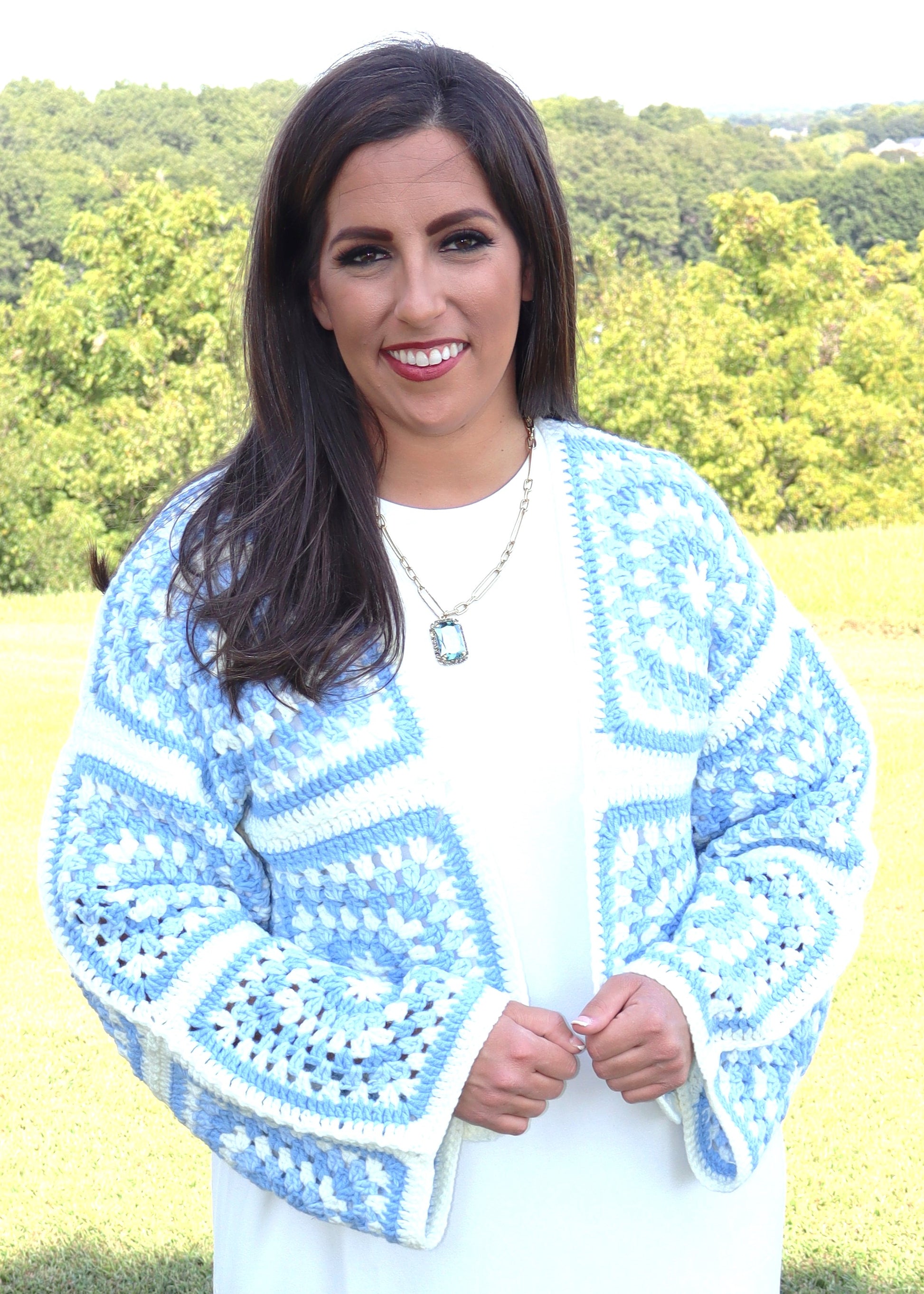 Woman wearing a blue and white crochet sweater in an outdoor setting.