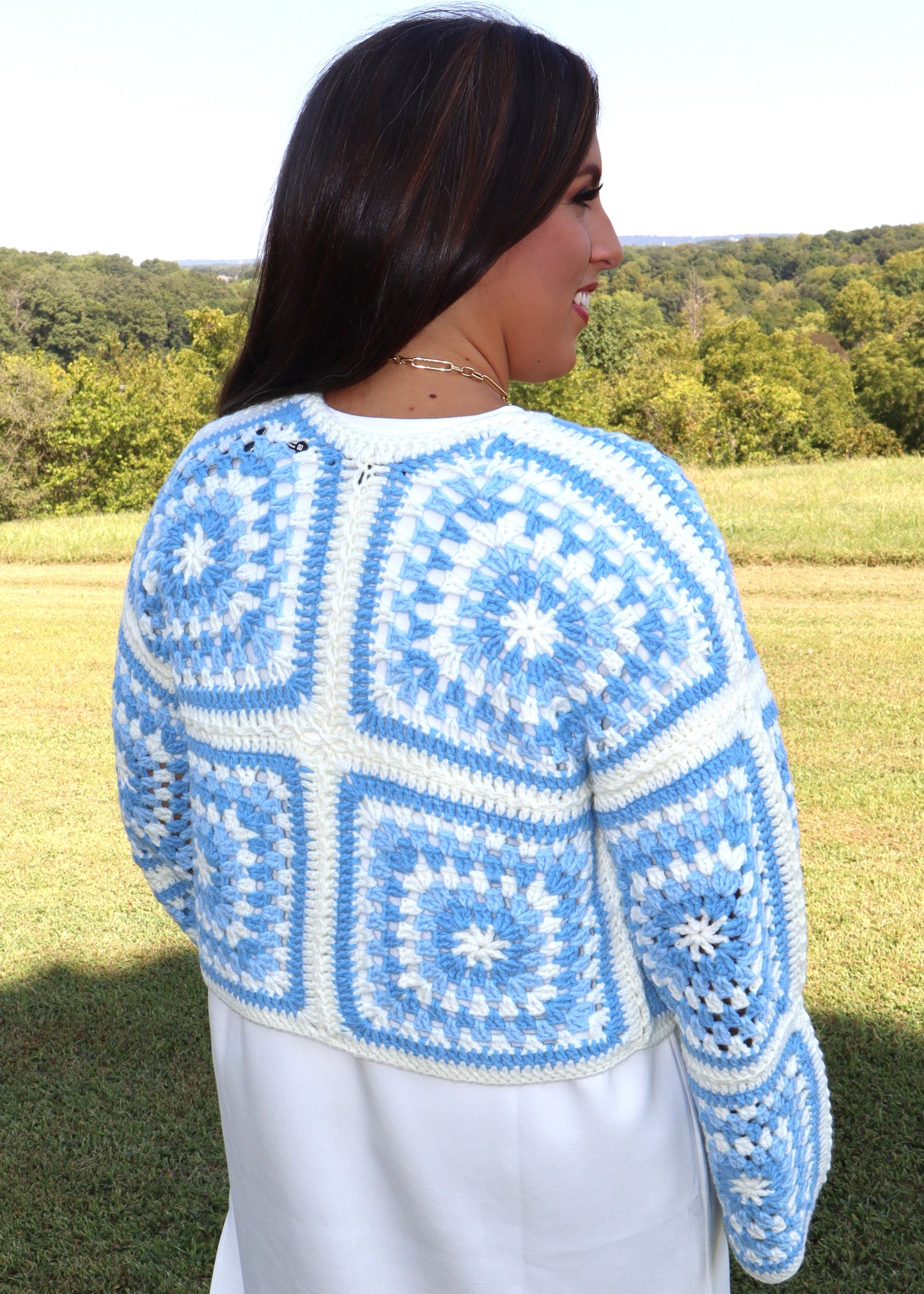 Woman wearing a blue and white crochet sweater in an outdoor setting.