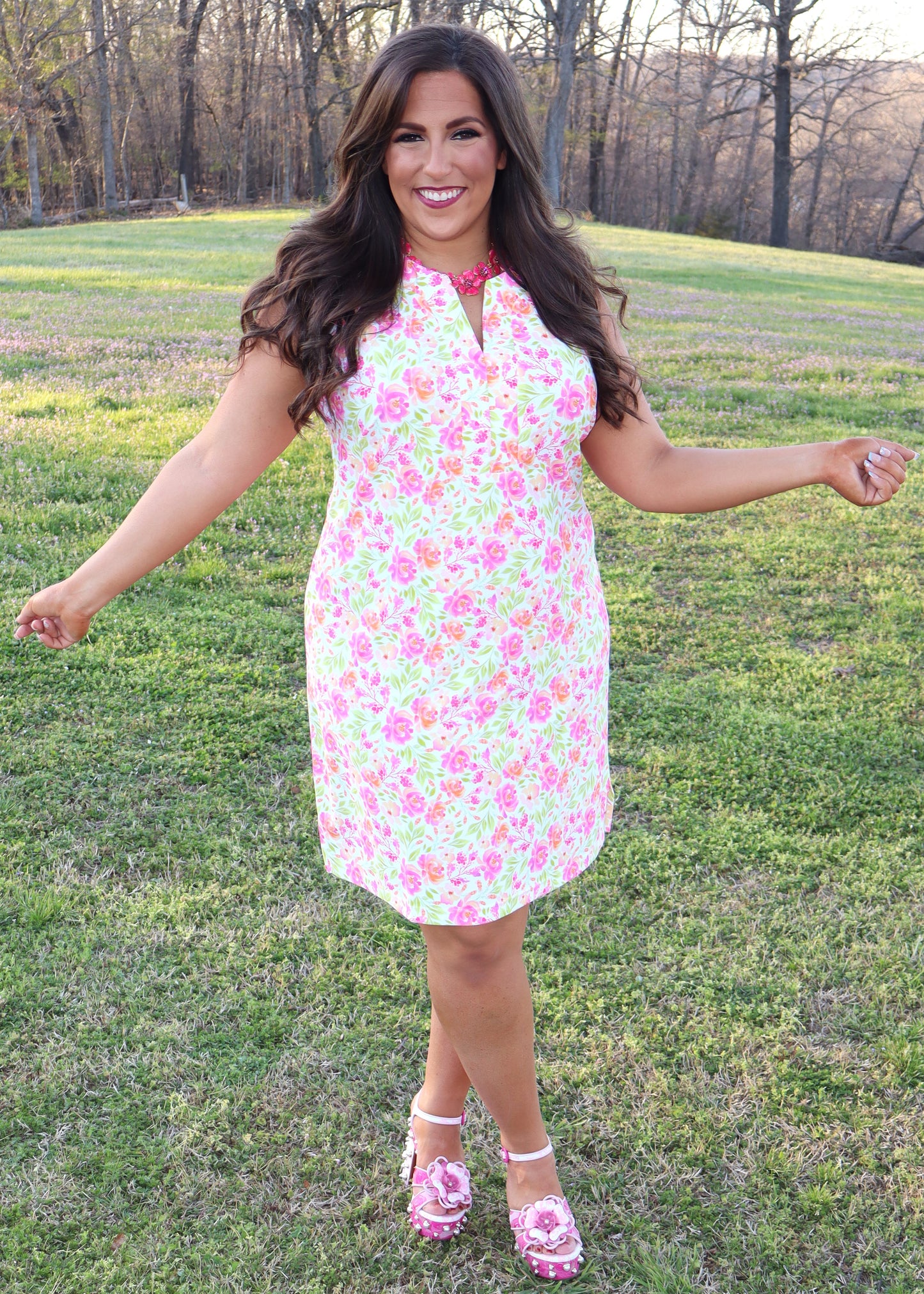 Woman wearing a white dress with neon floral print design standing in a grassy field