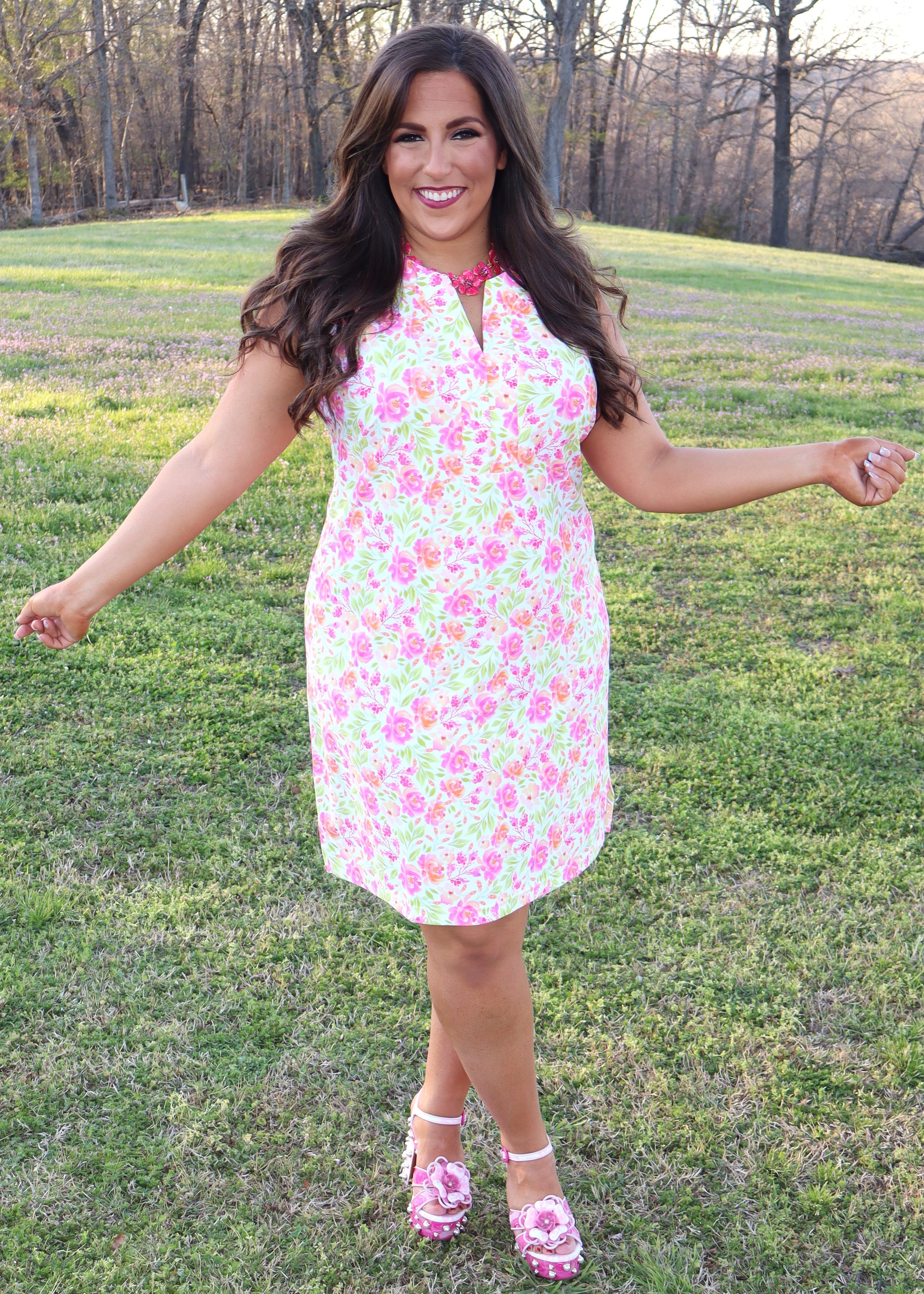 Woman wearing a white dress with neon floral print design standing in a grassy field
