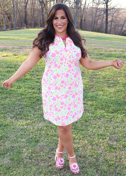 Woman wearing a white dress with neon floral print design standing in a grassy field