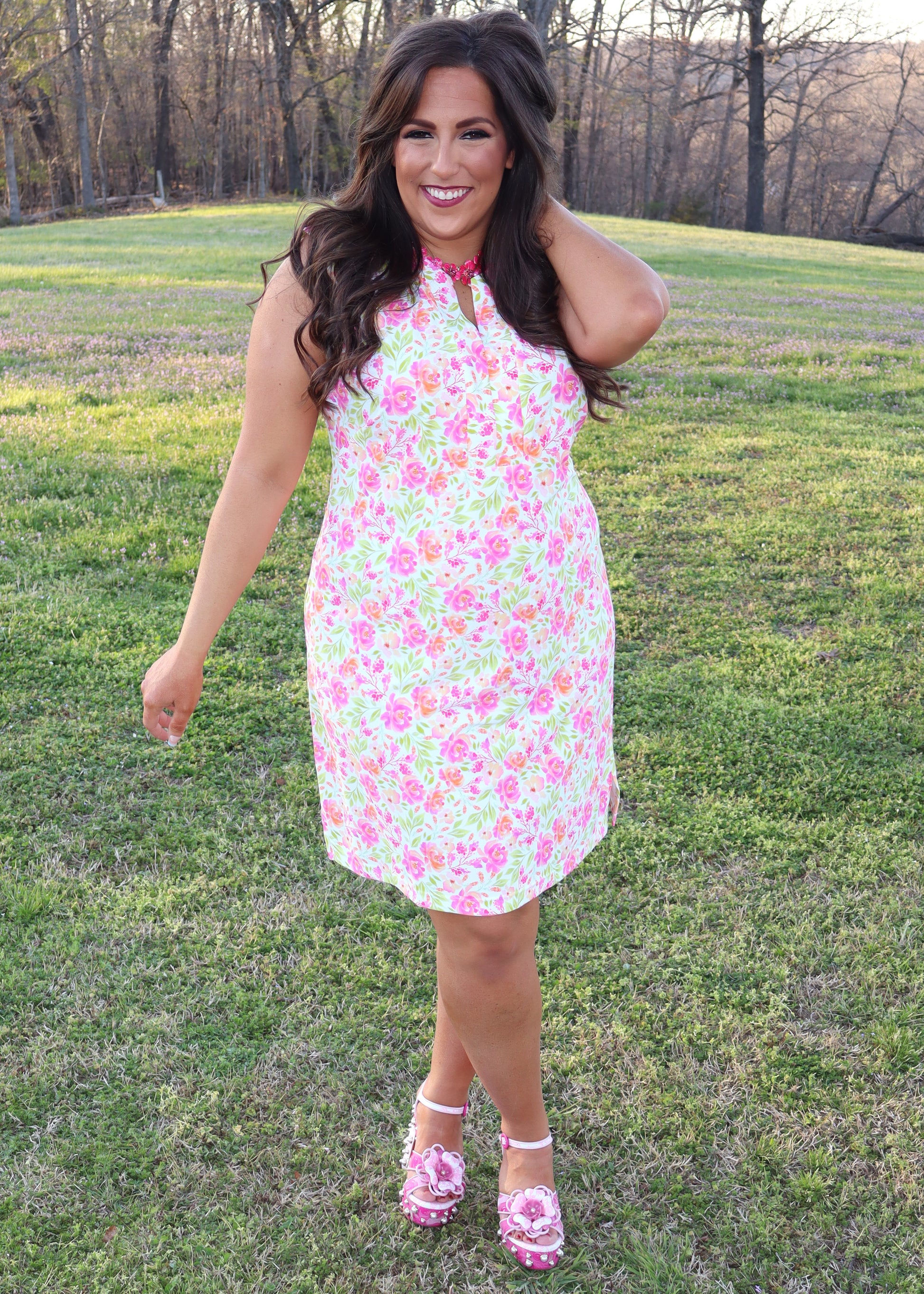 Woman wearing a white dress with neon floral print design standing in a grassy field
