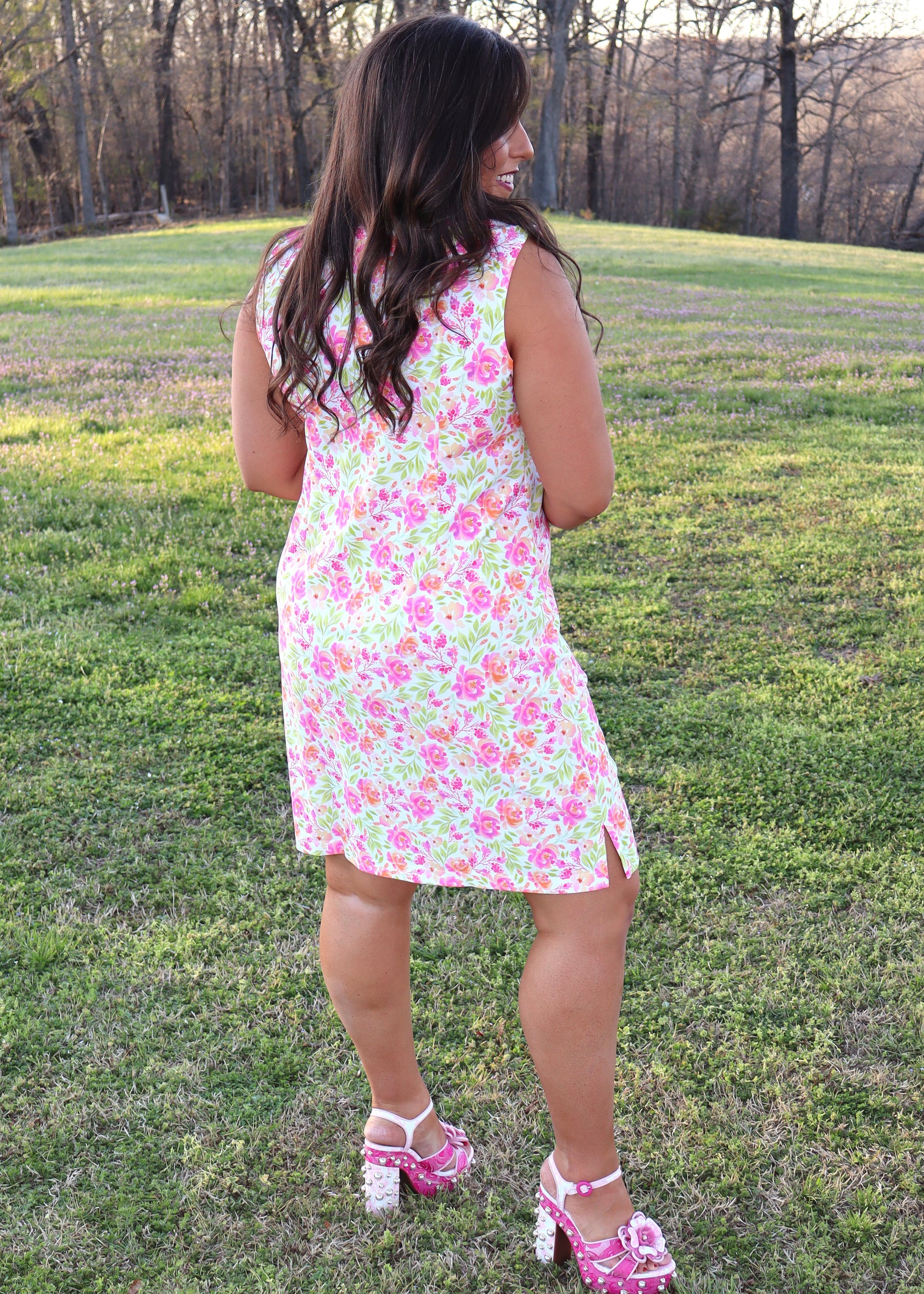 Woman wearing a white dress with neon floral print design standing in a grassy field