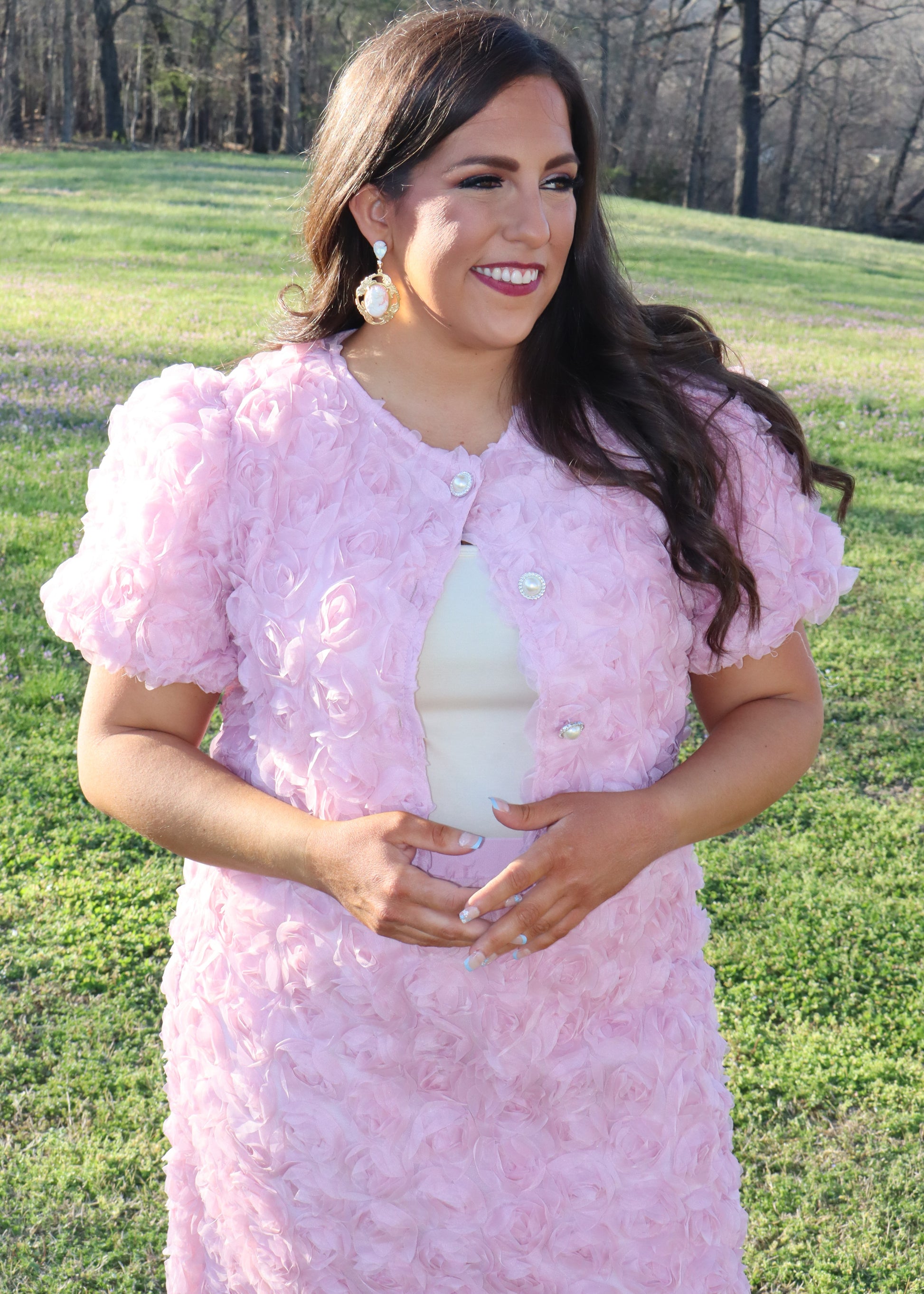 Woman wearing a pink matching skirt and tops with 3D floral sleeves standing in a grassy field.